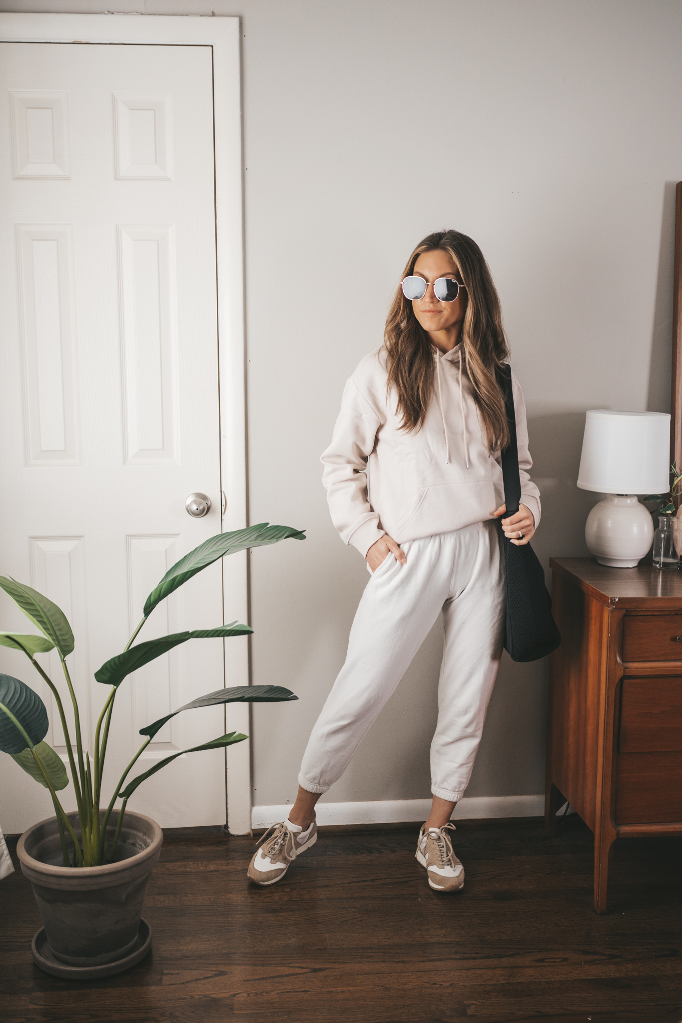 spring capsule wardrobe outfit with a taupe hoodie, white joggers, tan sneakers, and a black tote bag
