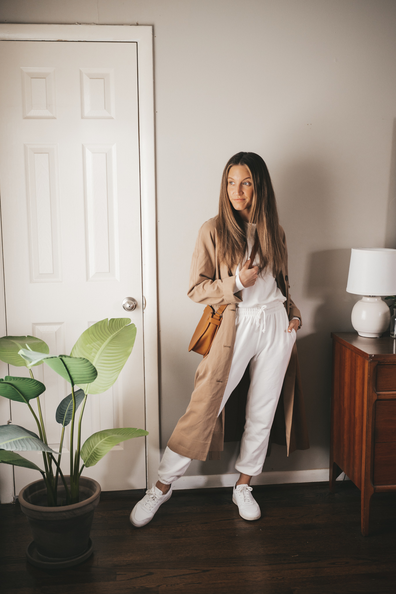 spring outfit with a white sweatsuit, white sneakers, tan trench coat and a cognac crossbody bag