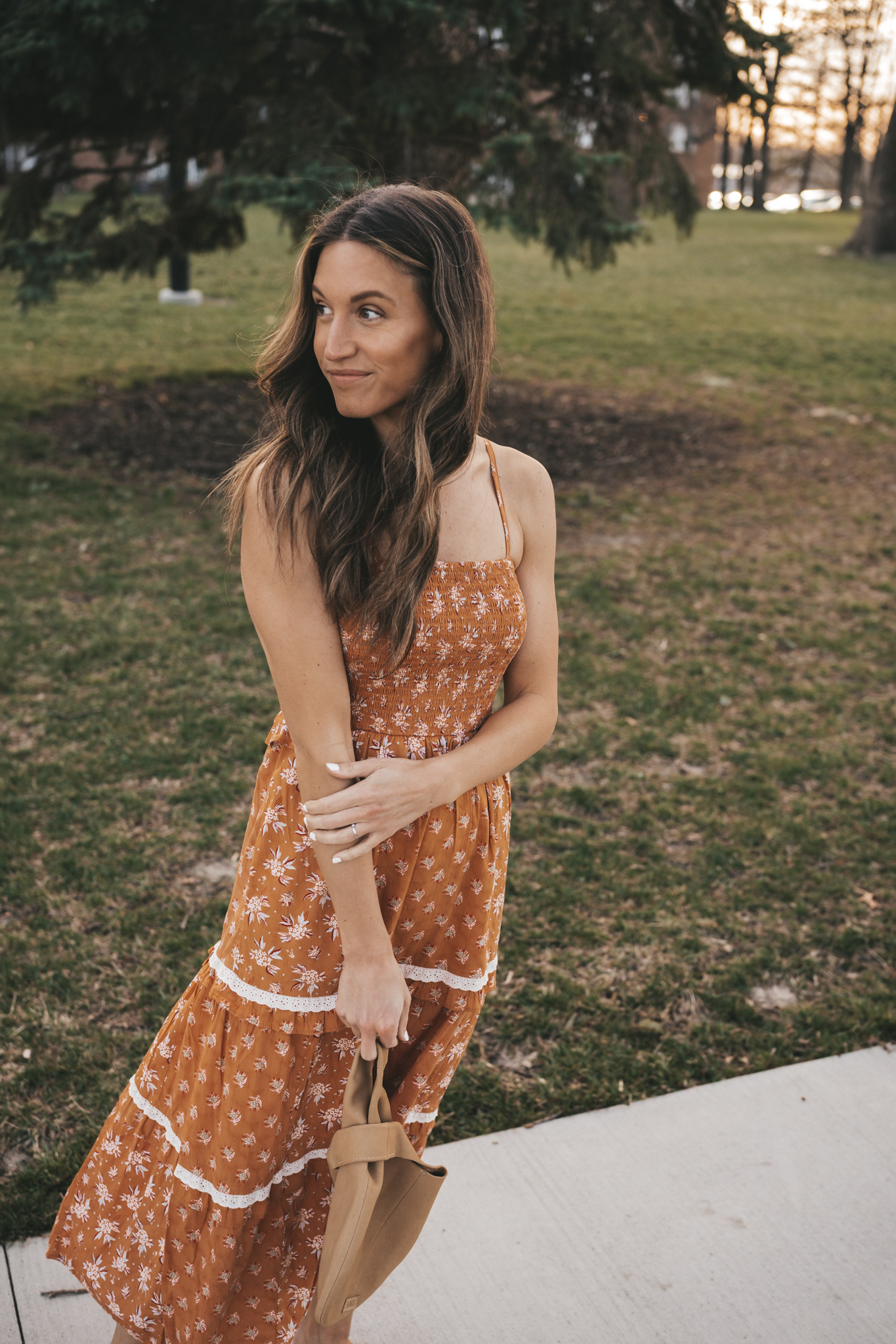 affordable spring dress or Easter dress; ashley wearing an orange floral patterned tiered midi dress standing on a sidewalk in a park