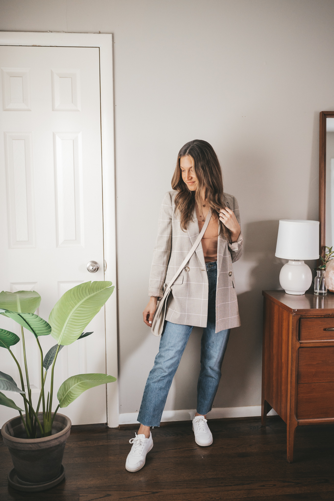 ashley wearing a blush tank, ivory plaid blazer, mid-wash straight denim, white sneakers, and a light gray crossbody bag