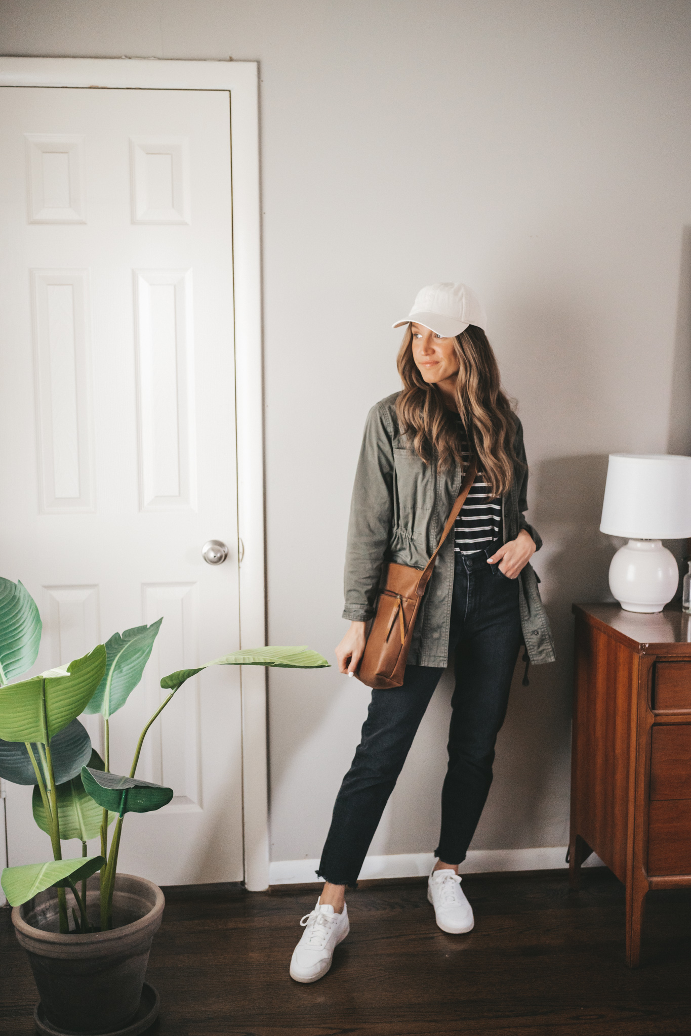 ashley wearing a white and black striped tee, green utility jacket, black mom jeans, white sneakers, and a brown crossbody bag