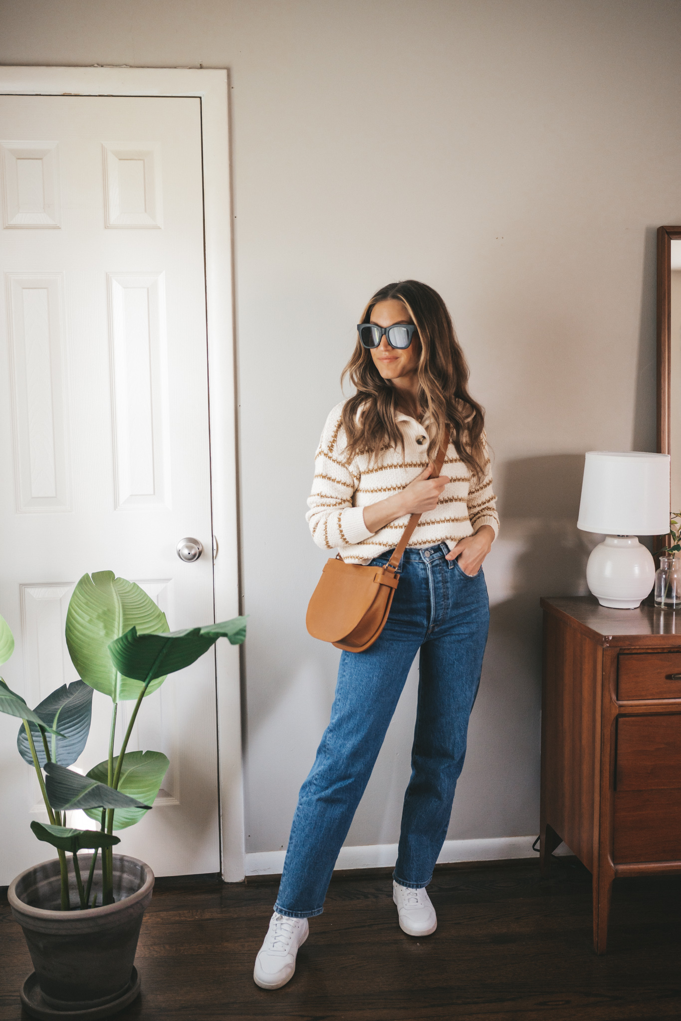 spring outfit idea with a striped ivory sweater, mid-wash denim, white sneakers, and a cognac crossbody bag