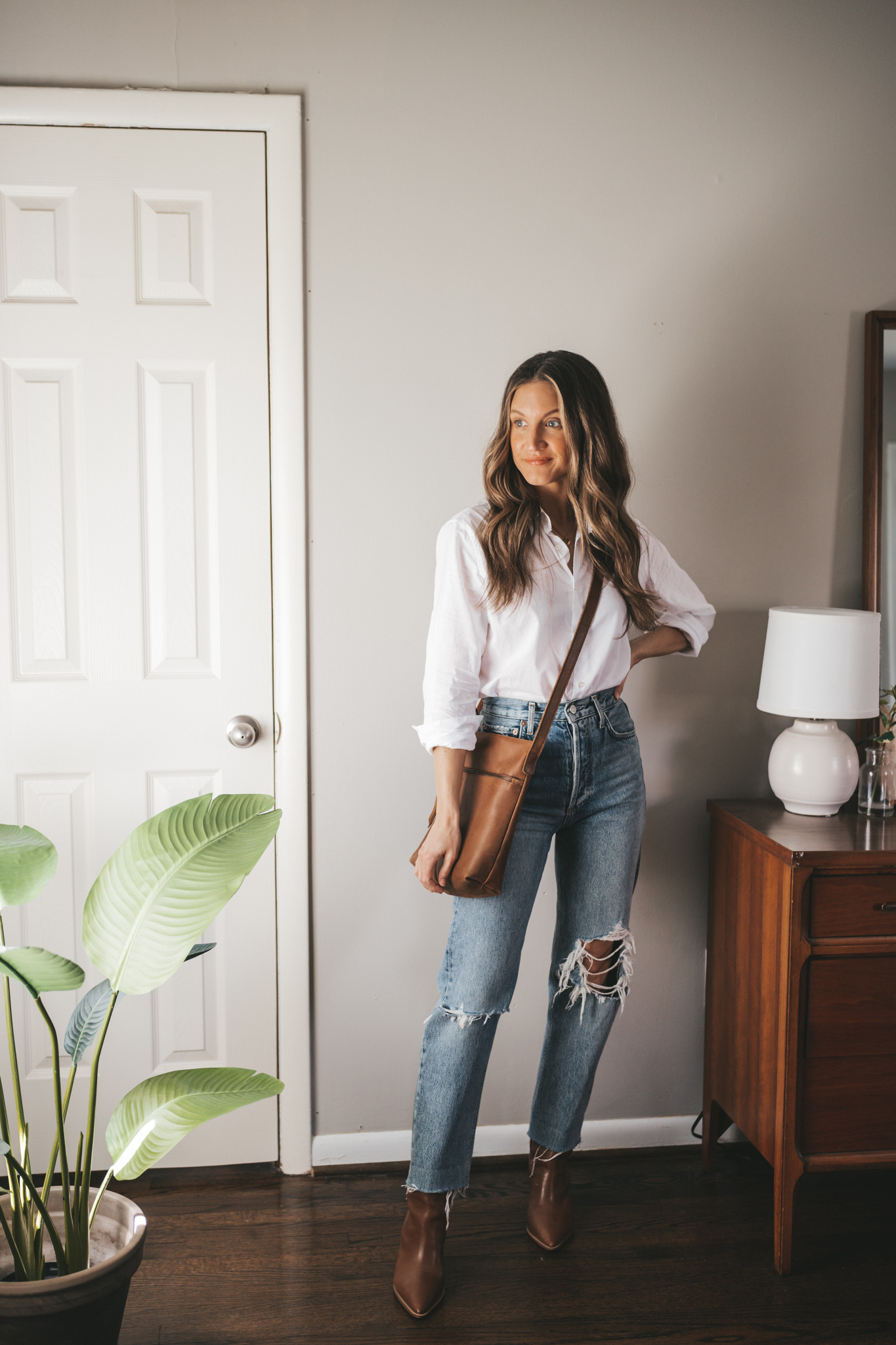 ashley wearing a white button down, distressed denim, brown ankle boots, and a brown crossbody bag