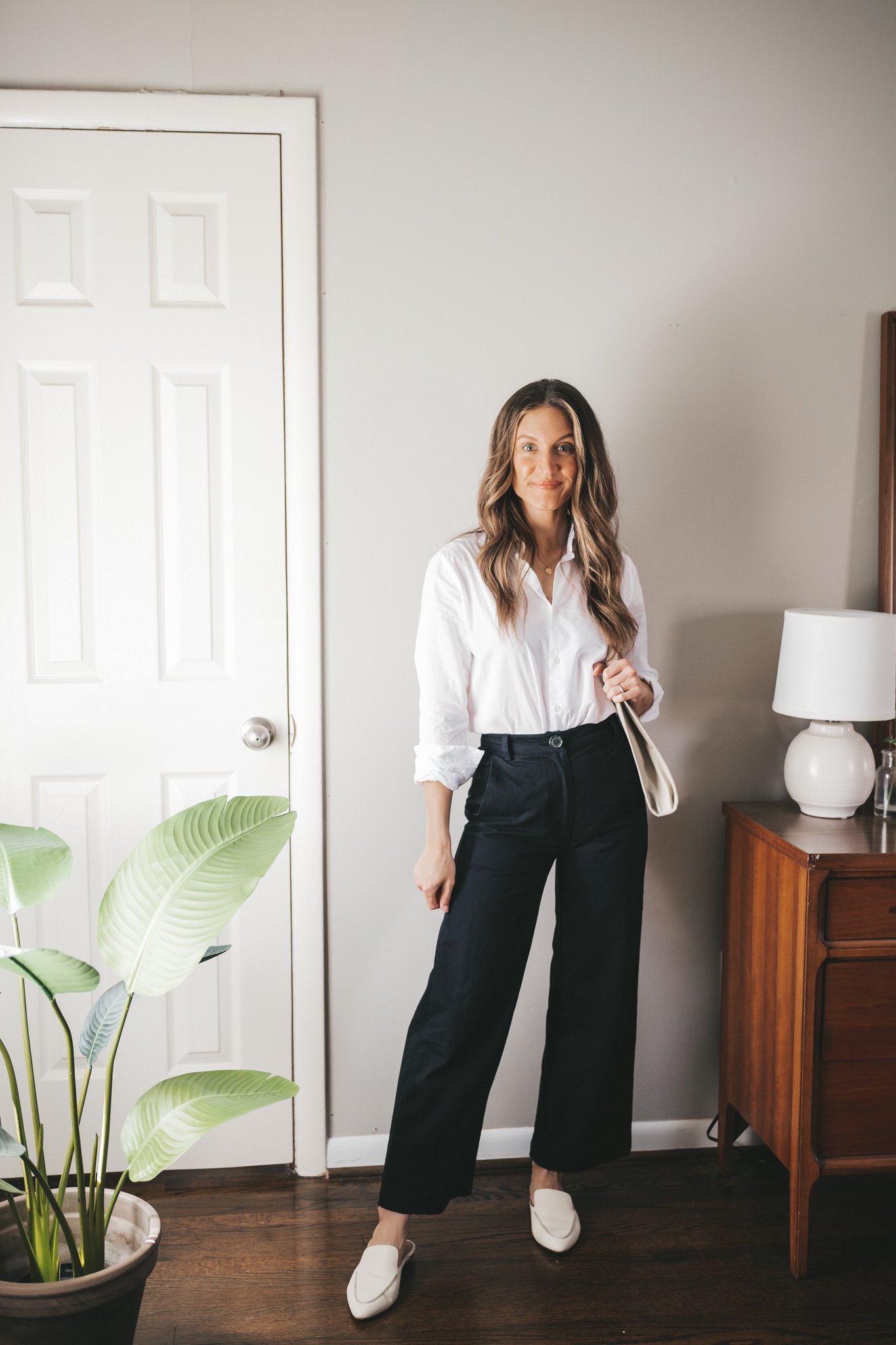 ashley wearing a white button down, black wide leg pants, white mules, and a light gray shoulder bag