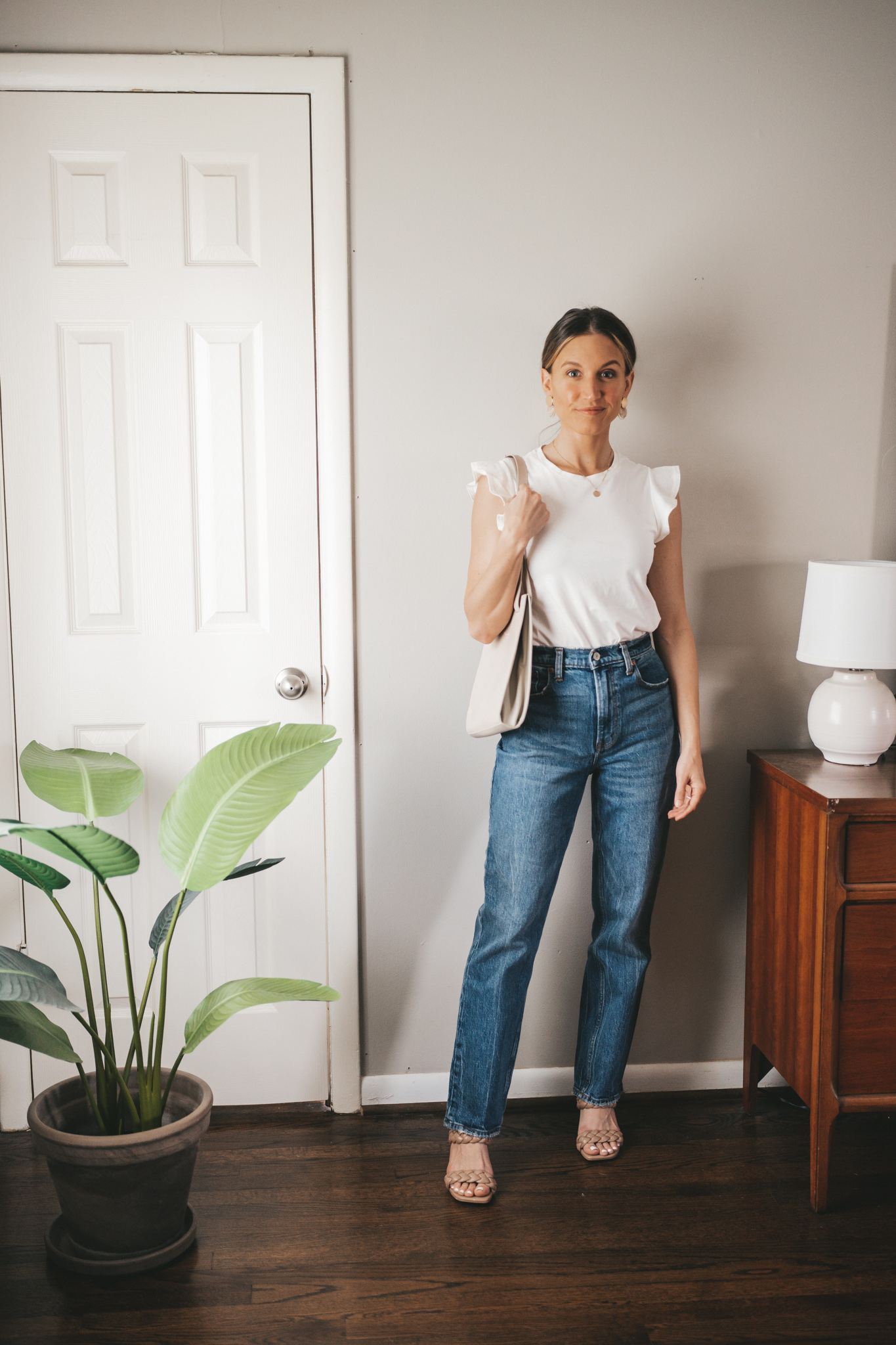 spring outfit idea with a white tee with ruffled sleeves, mid-wash denim, braided taupe two strap sandals, and a gray shoulder bag