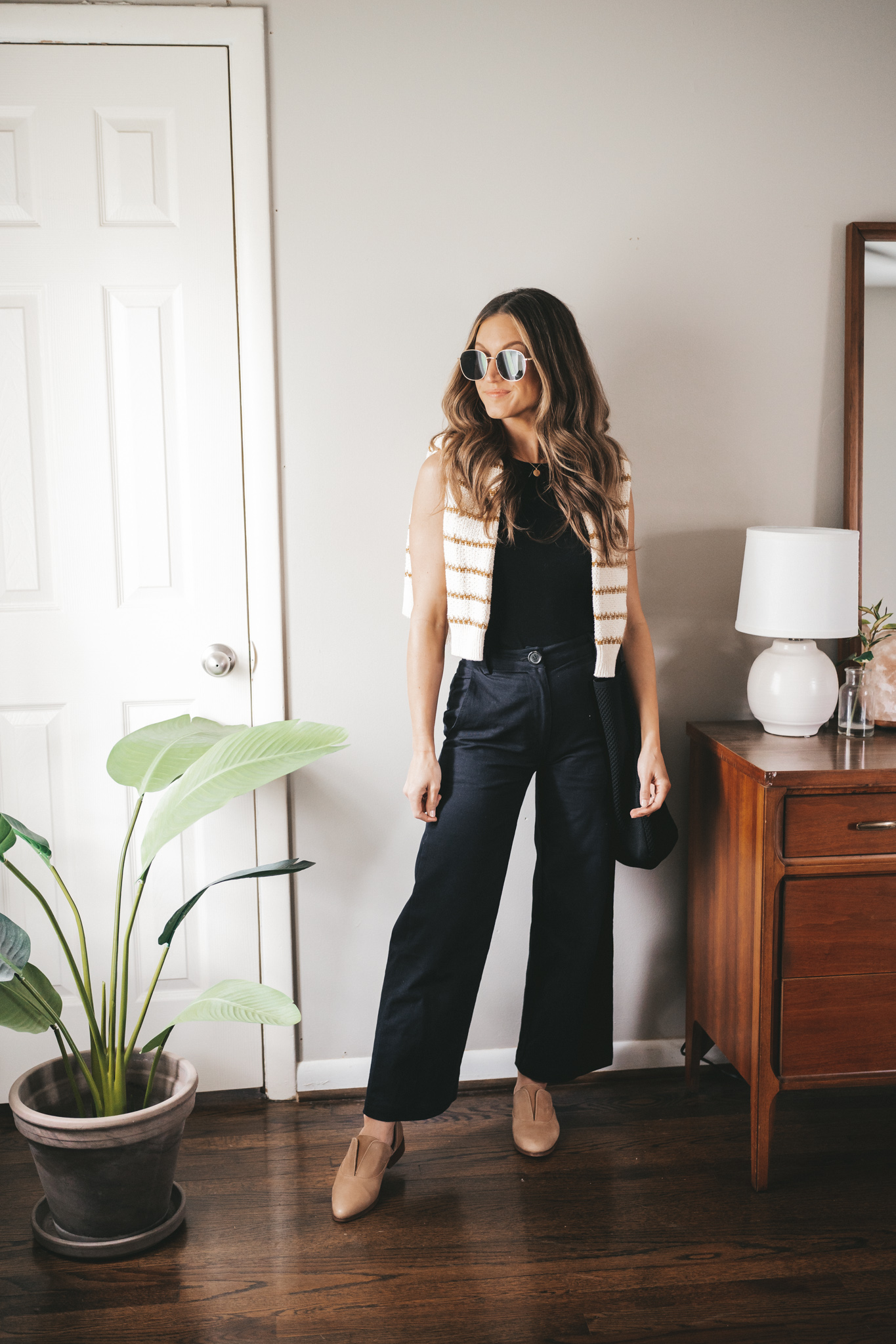 spring outfit with a black tank and a striped sweater worn over the shoulders, black wide leg cropped pants, and nude oxfords with gold framed sunglasses