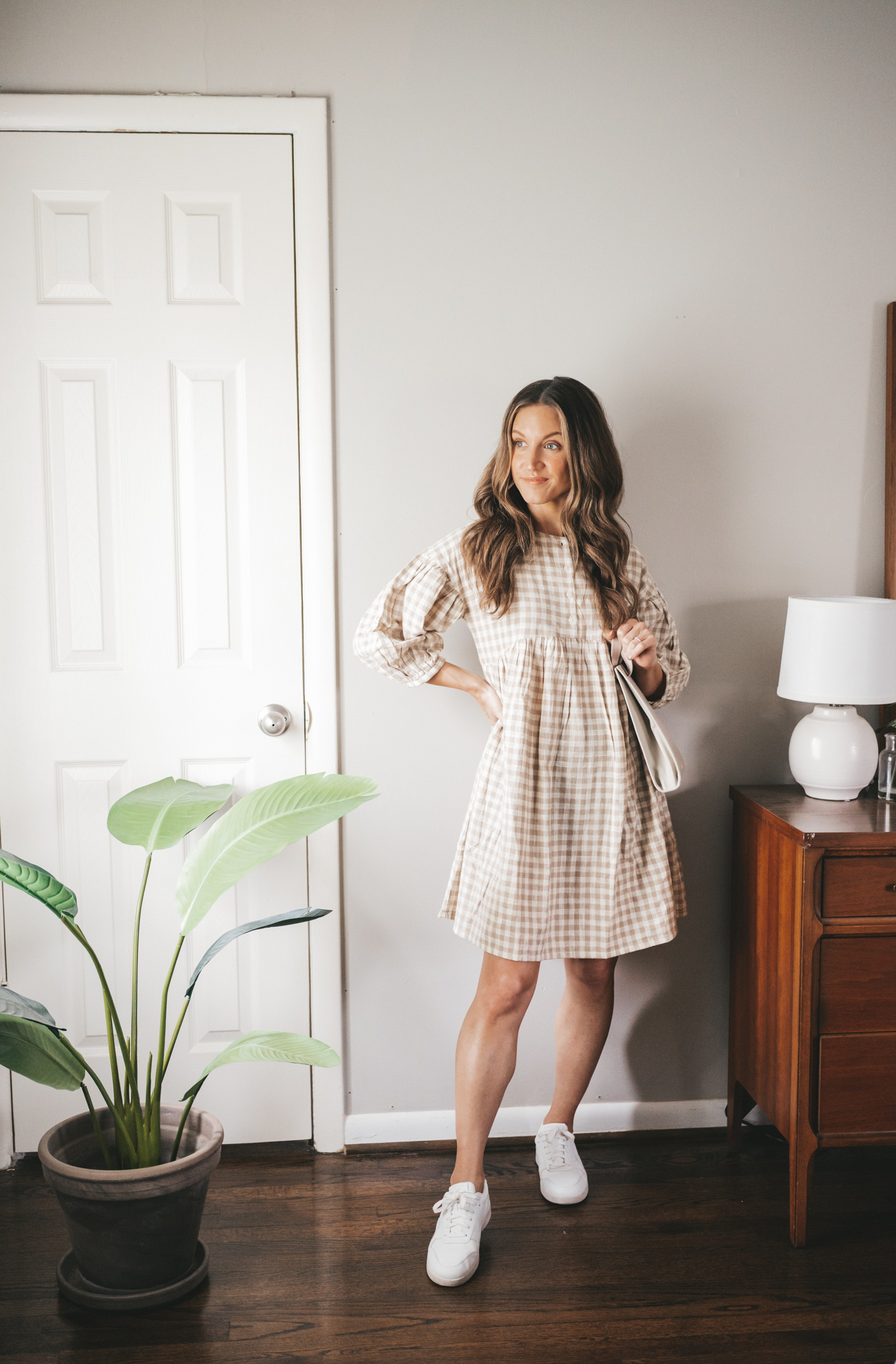 spring outfit with a tan and white gingham swing dress, white sneakers, and a gray shoulder bag