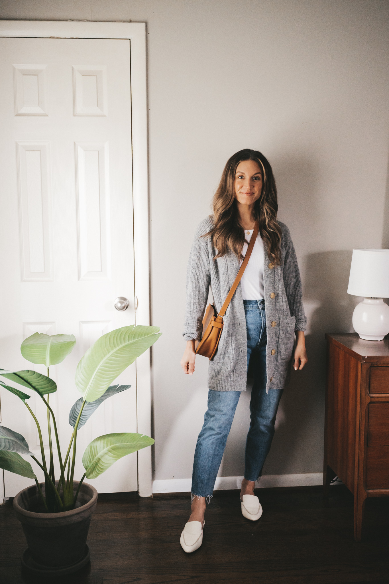 spring outfit with a white tank, gray thigh length cardigan, and mid-wash straight leg denim with a cognac crossbody bag