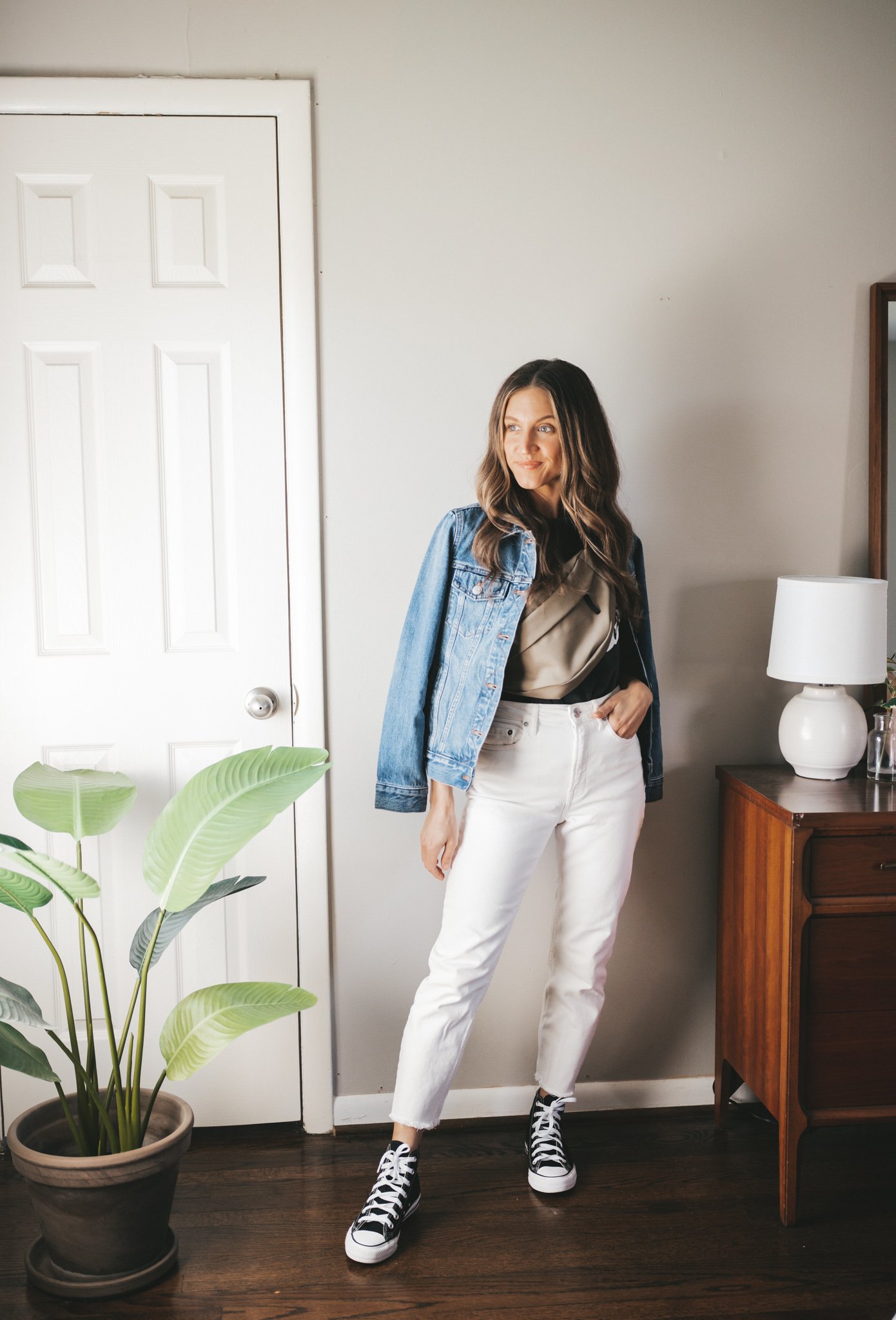 white denim outfit idea with a black graphic tee, denim jacket, white denim, black high top Converse and an olive green belt bag