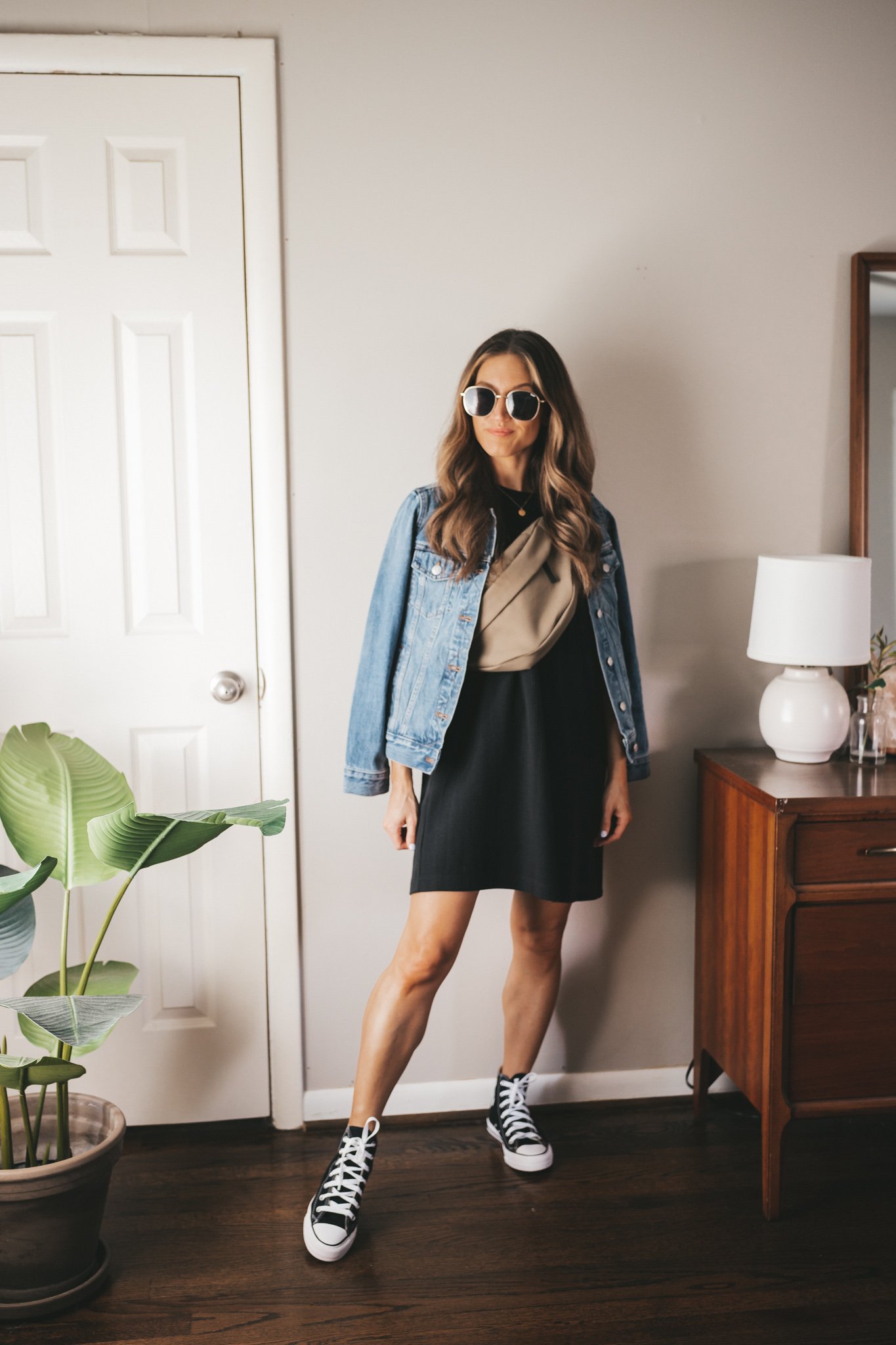 ashley wearing a black t-shirt dress, denim jacket, olive green belt bag, and black high top Converse