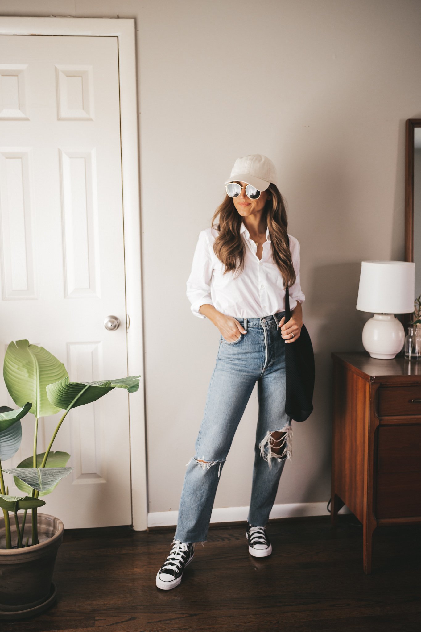 ashley wearing a white button down, distressed denim, ivory baseball cap, and black high top Converse