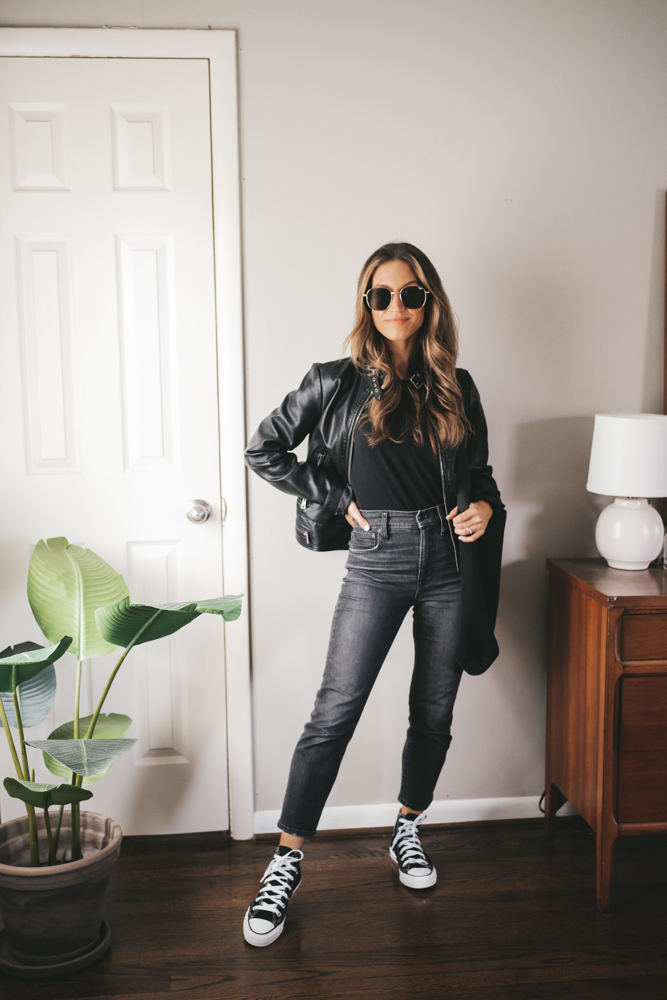 ashley wearing a black tank, black moto jacket, washed black denim, and black high top Converse
