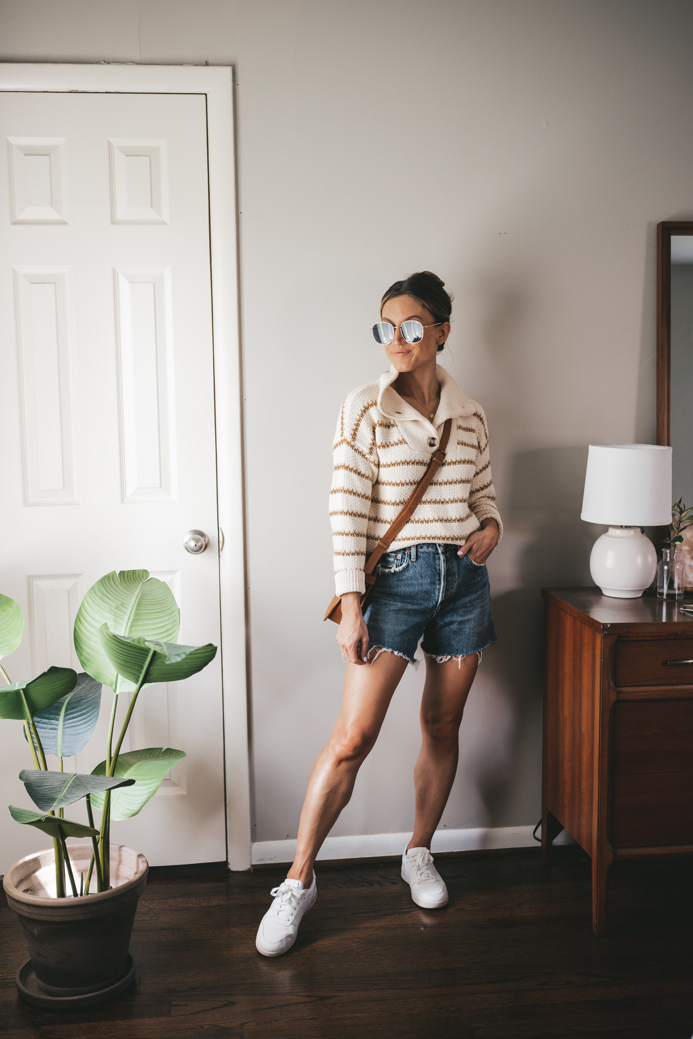 outfit for spring with an ivory and green striped sweater, cut-off denim shorts, and white sneakers