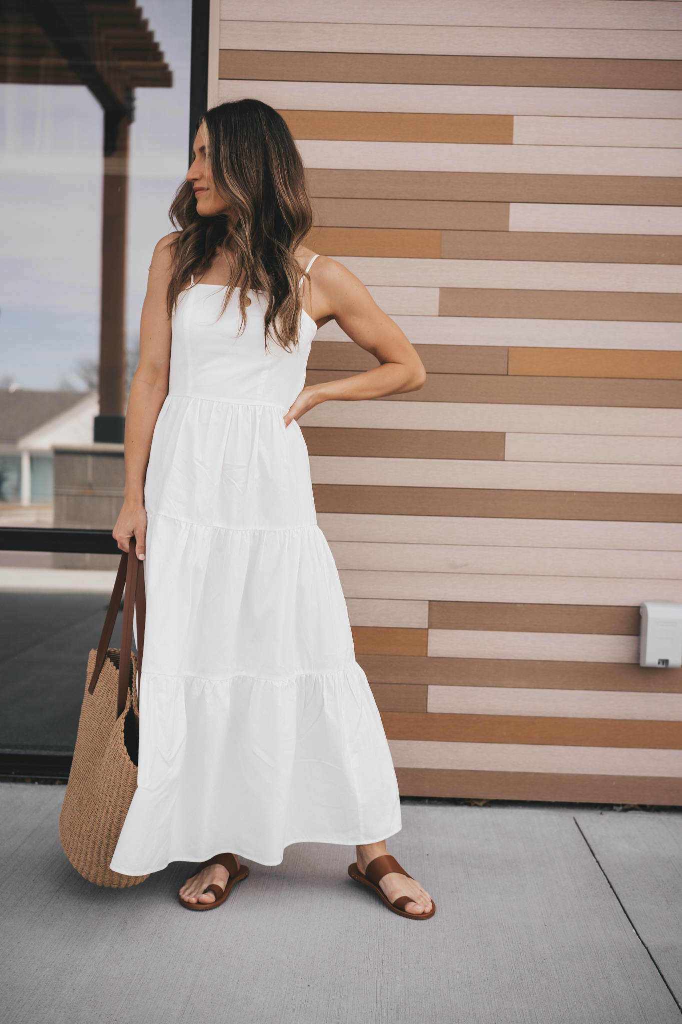 ashley wearing a white midi dress, brown leather sandals, and a straw tote bag