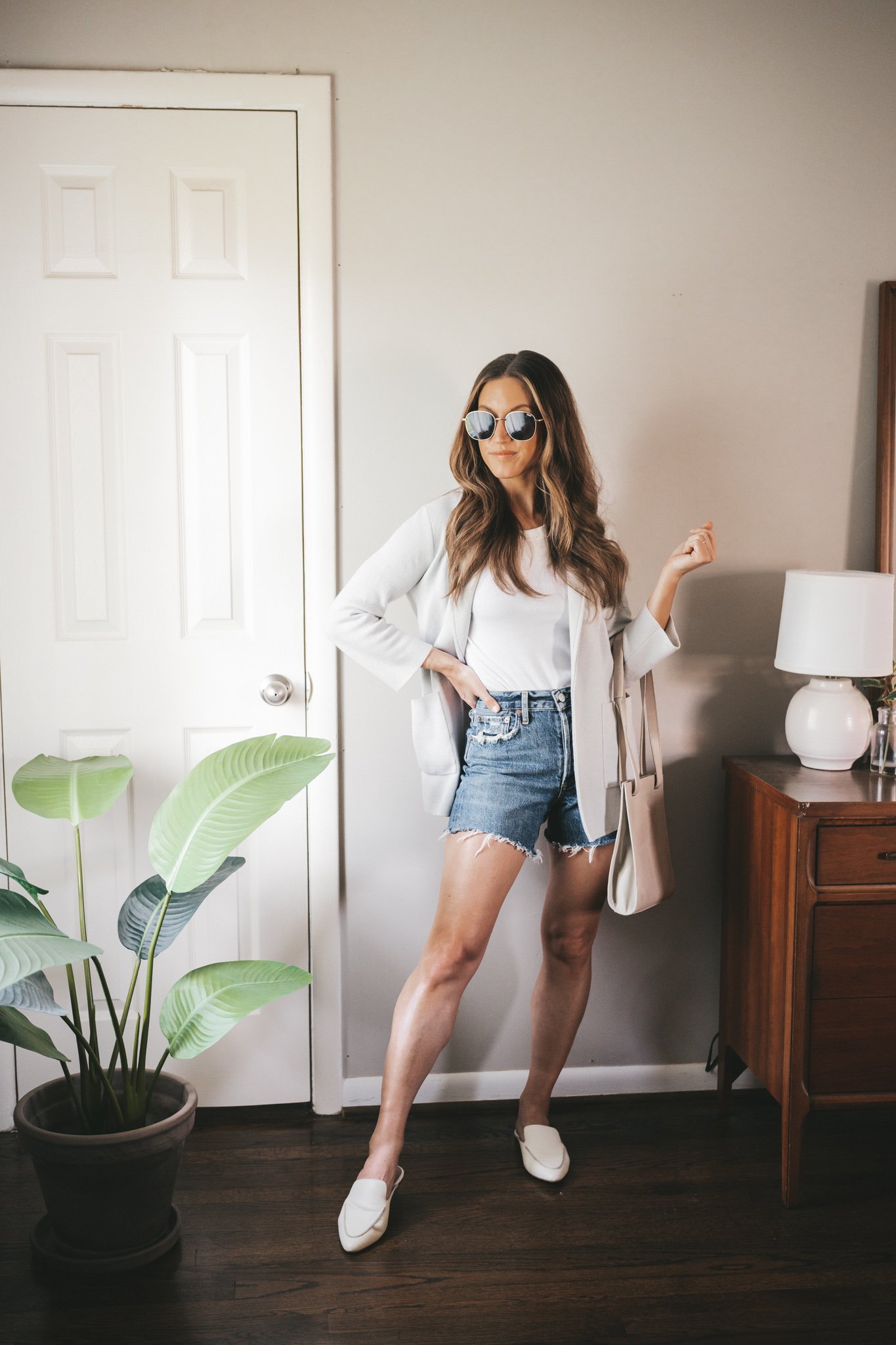 ashley wearing a white tank, gray sweater blazer, cut-off denim shorts, and white mules with a gray crossbody bag