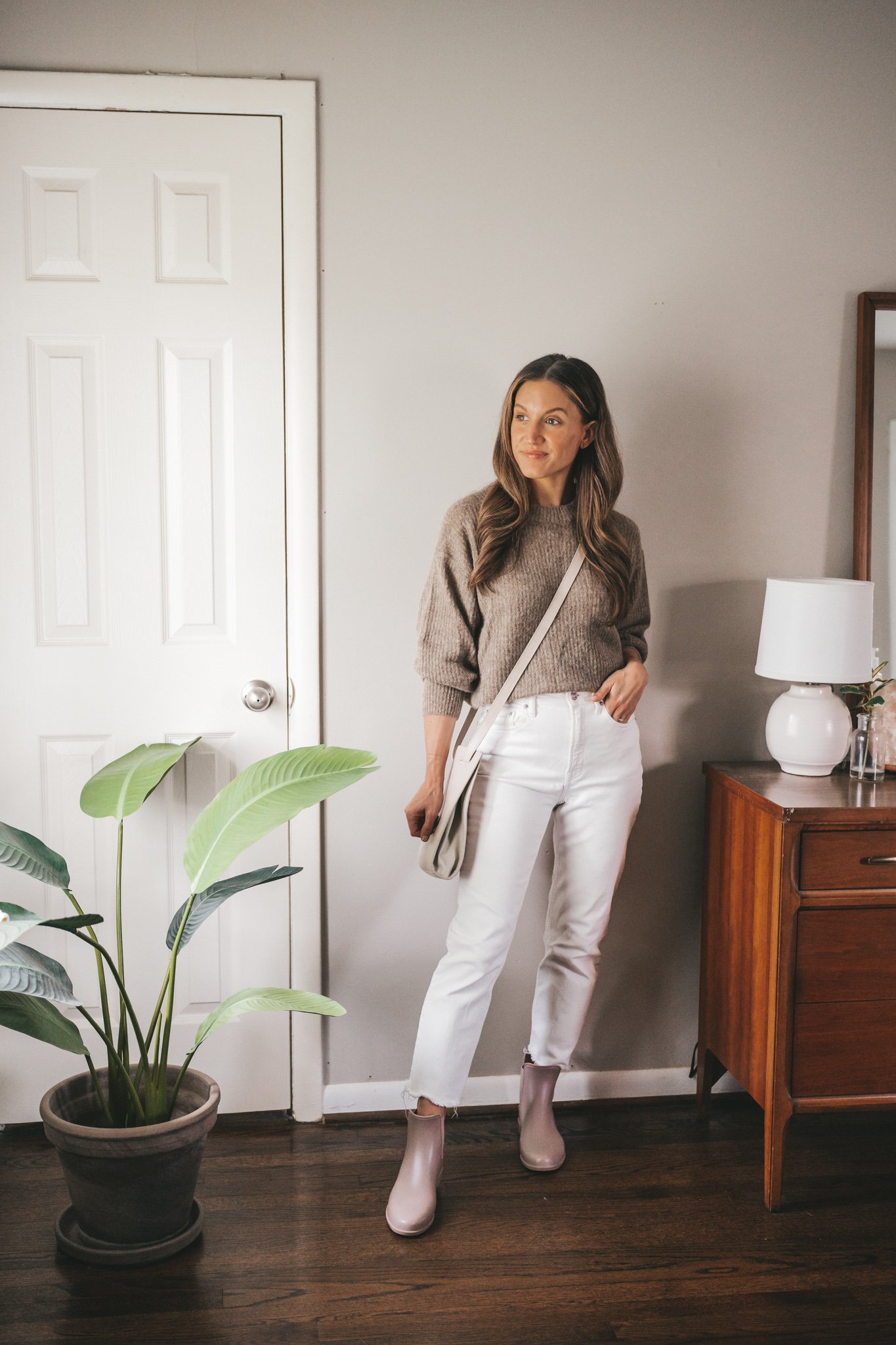 ashley wearing a taupe sweater, white straight denim, taupe rainboots and a light gray leather crossbody bag