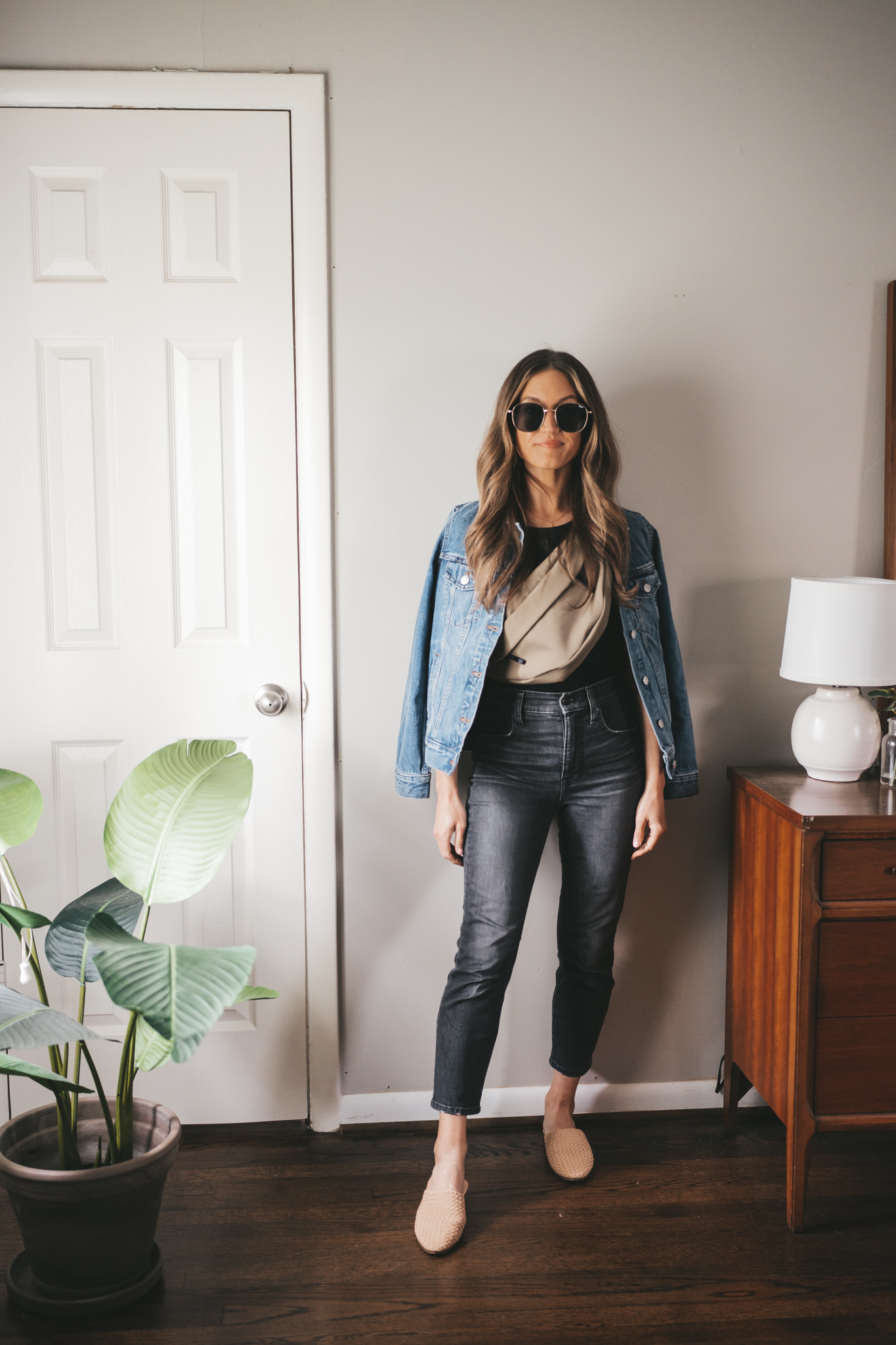 ashley wearing a black tank, denim jacket, olive green belt bag, washed black denim, and woven mules