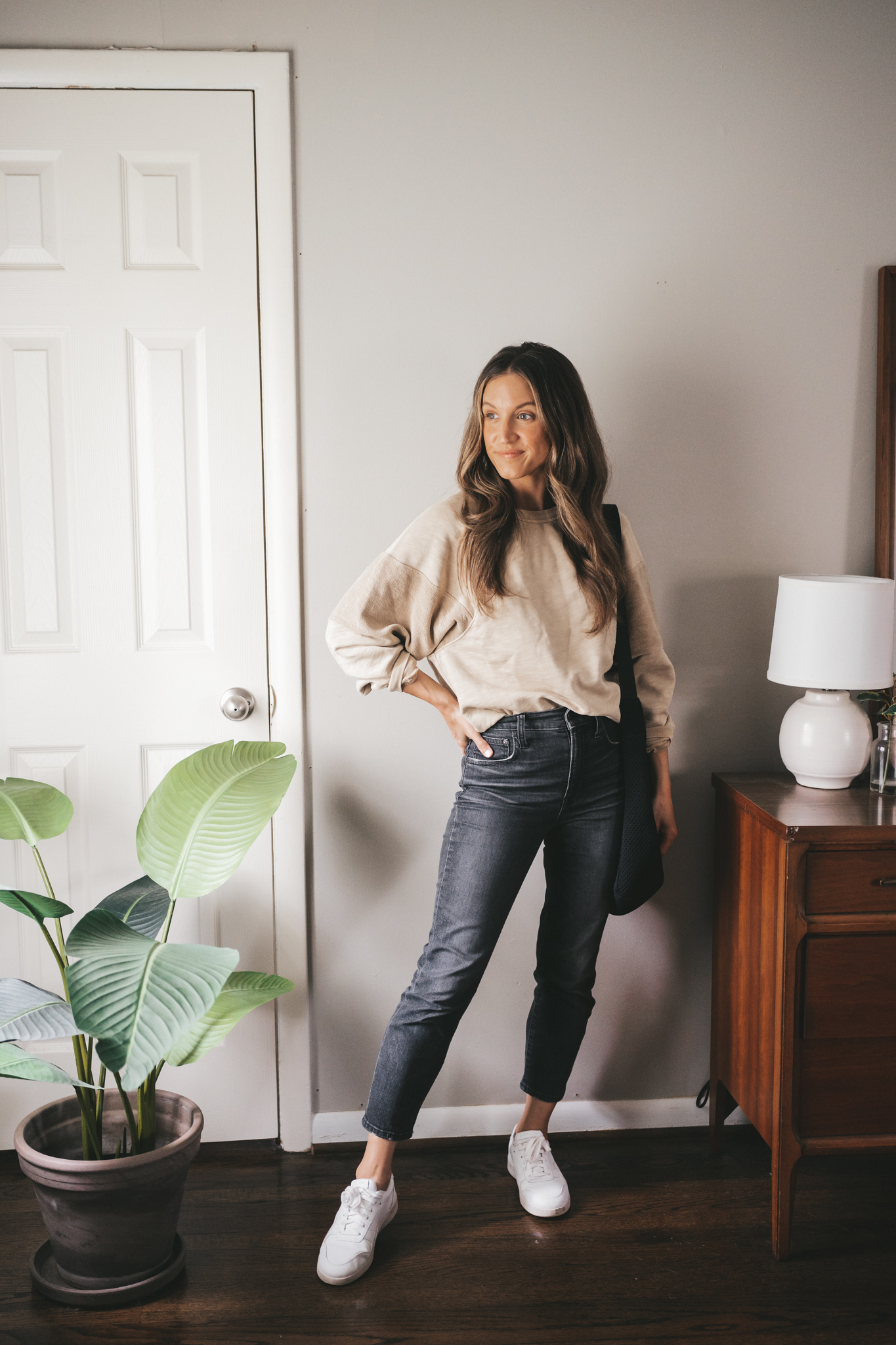 ashley wearing a tan oversized sweatshirt, washed black denim, and white sneakers with a black tote bag
