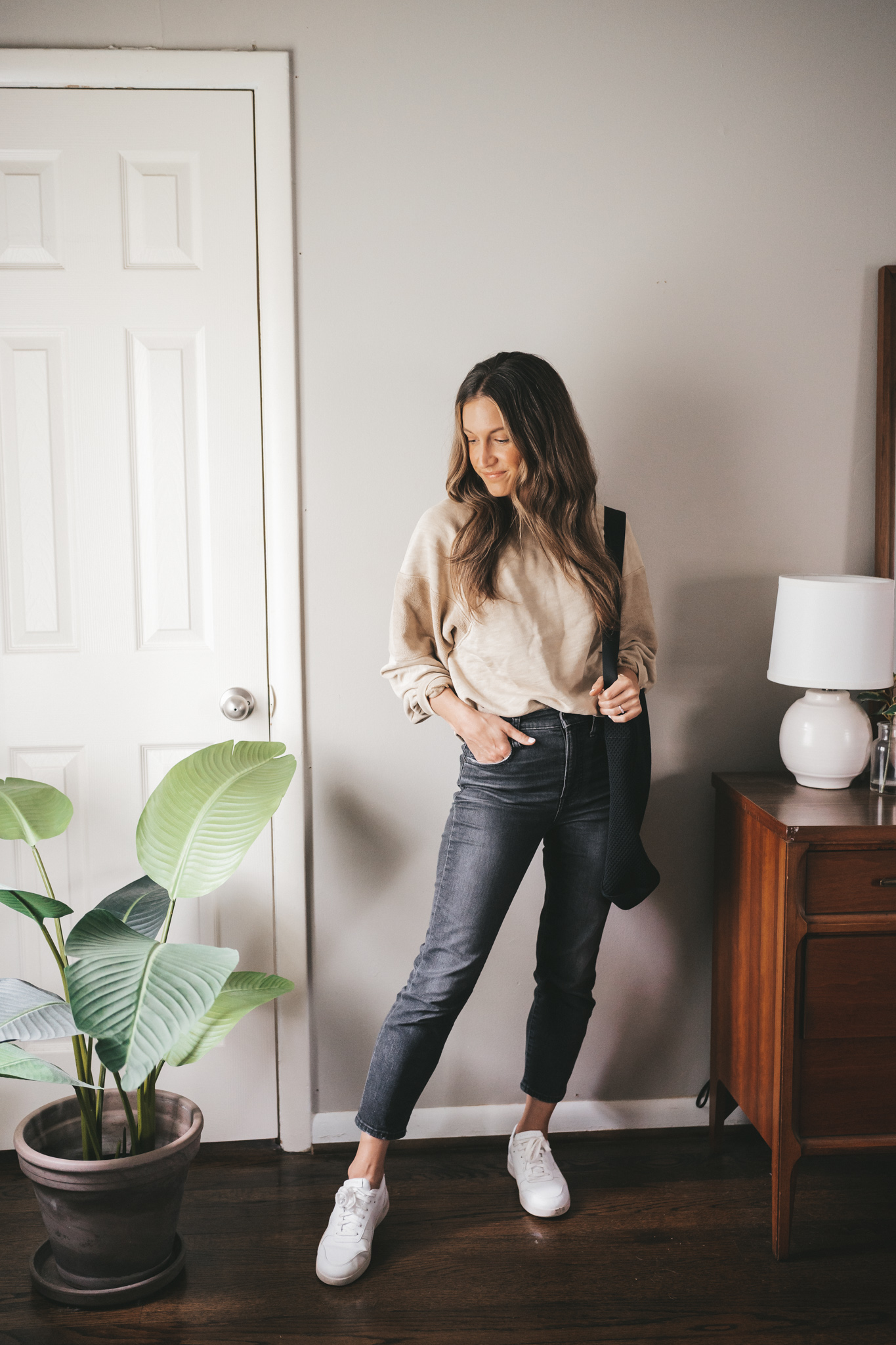 ashley wearing a tan oversized sweatshirt, washed black denim, and white sneakers with a black tote bag