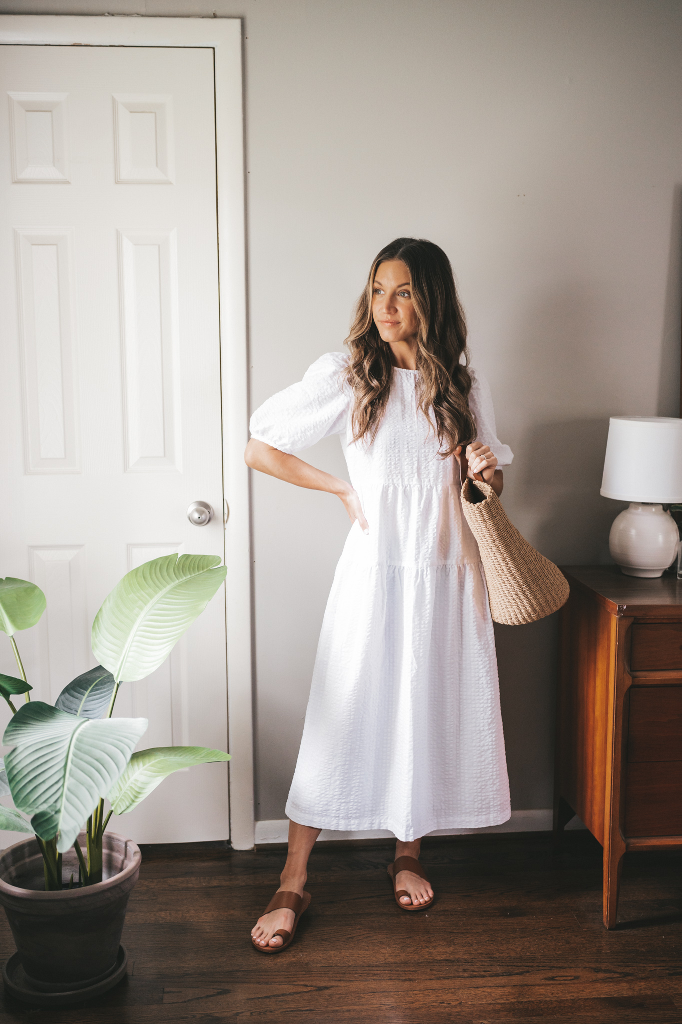 ashley wearing a white puff sleeve tiered midi dress with brown leather toe ring sandals and a straw tote bag