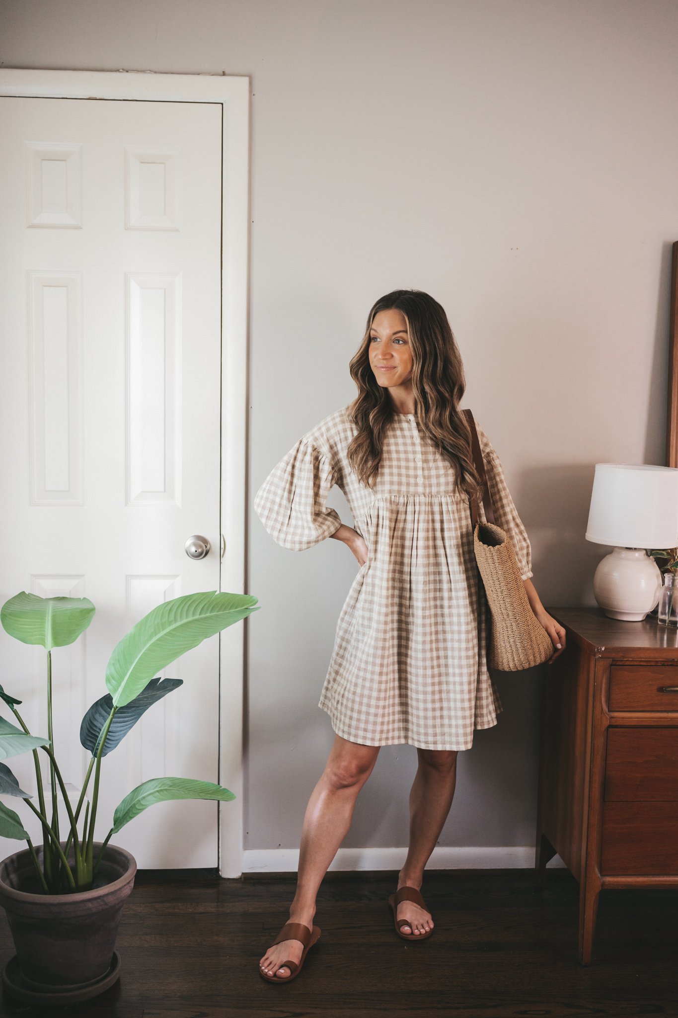 ashley wearing a white and tan gingham mini dress, straw tote bag and brown leather sandals