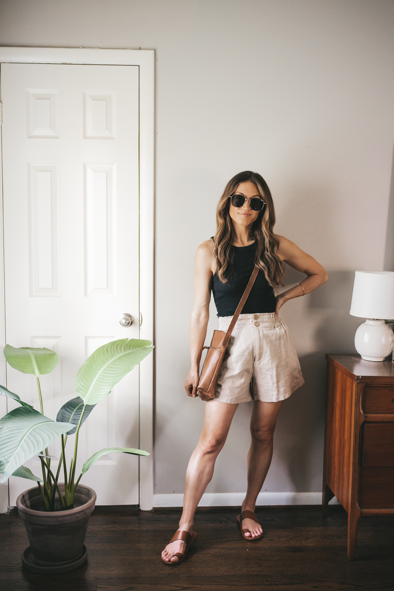 ashley wearing a black tank, tan linen shorts, brown leather sandals, and a brown leather crossbody bag