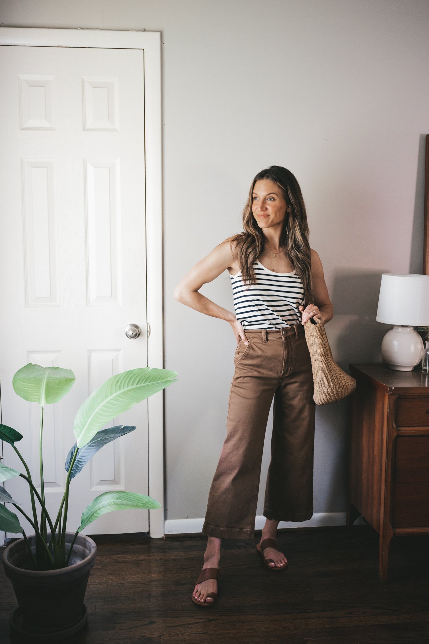 how to wear a striped tank; ashley wearing a striped tank with brown wide leg cropped pants, brown leather sandals, and a straw tote bag