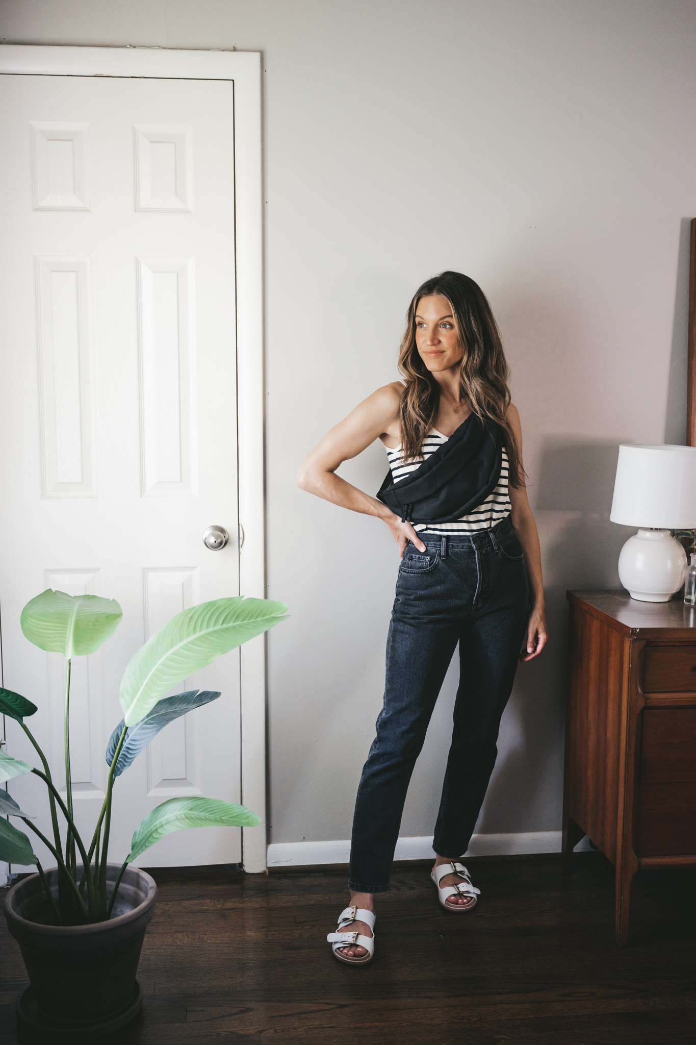 ashley wearing a white and navy striped tank, black denim, white two strap footbed sandals, and a black belt bag