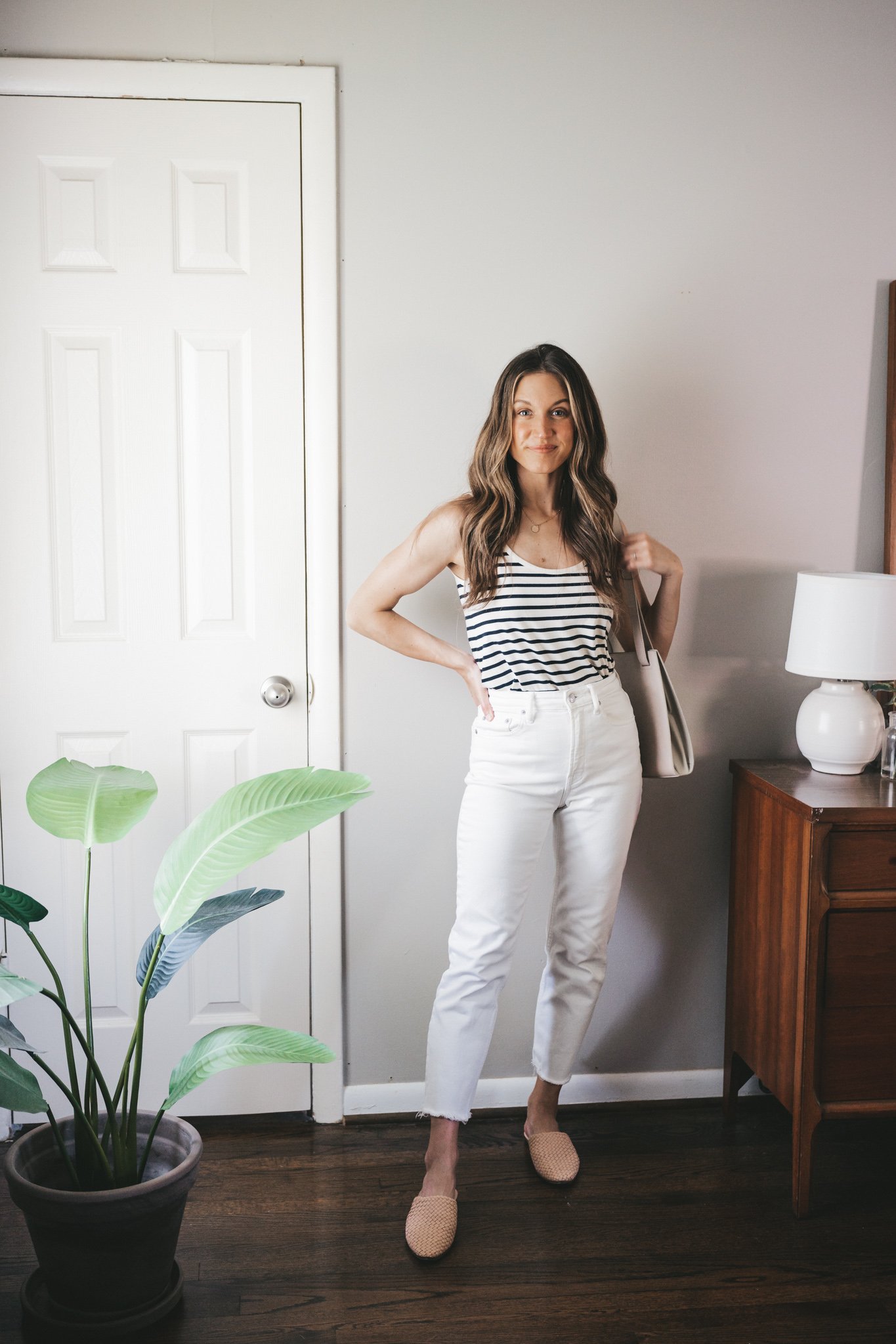 ashley wearing a white and navy striped tank, white denim, tan woven mules, and a gray shoulder bag