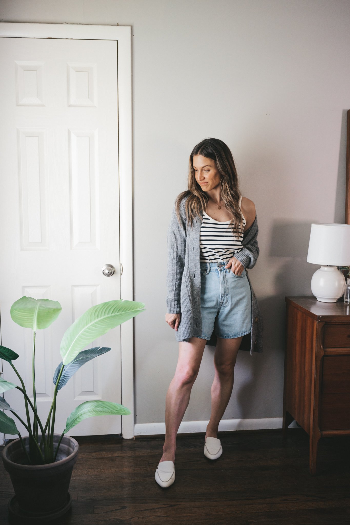 how to wear a striped tank; ashley wearing a navy and white striped tank, light wash denim shorts, an oversized gray cardigan, and white mules