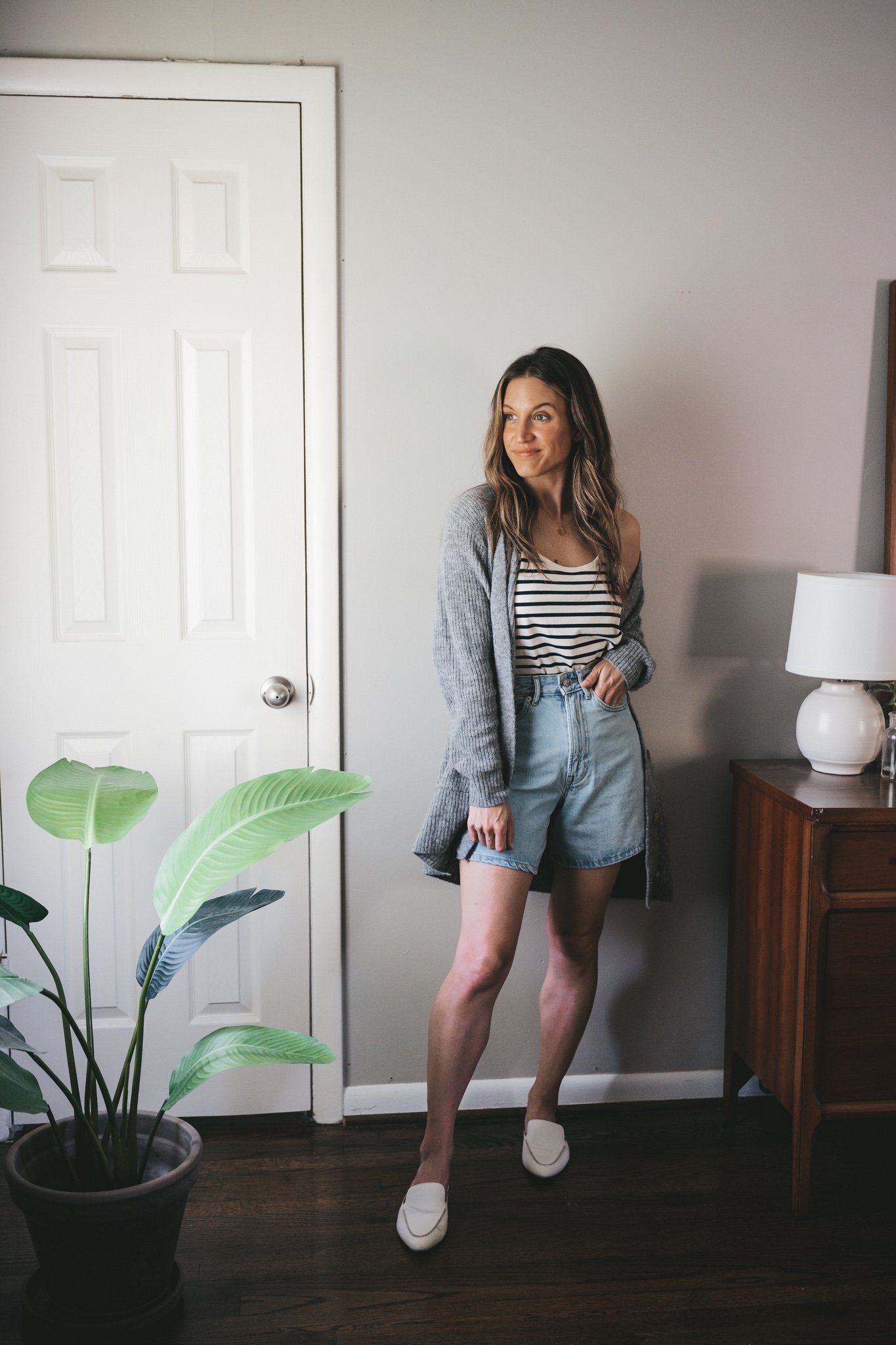 how to wear a striped tank; ashley wearing a navy and white striped tank, light wash denim shorts, an oversized gray cardigan, and white mules