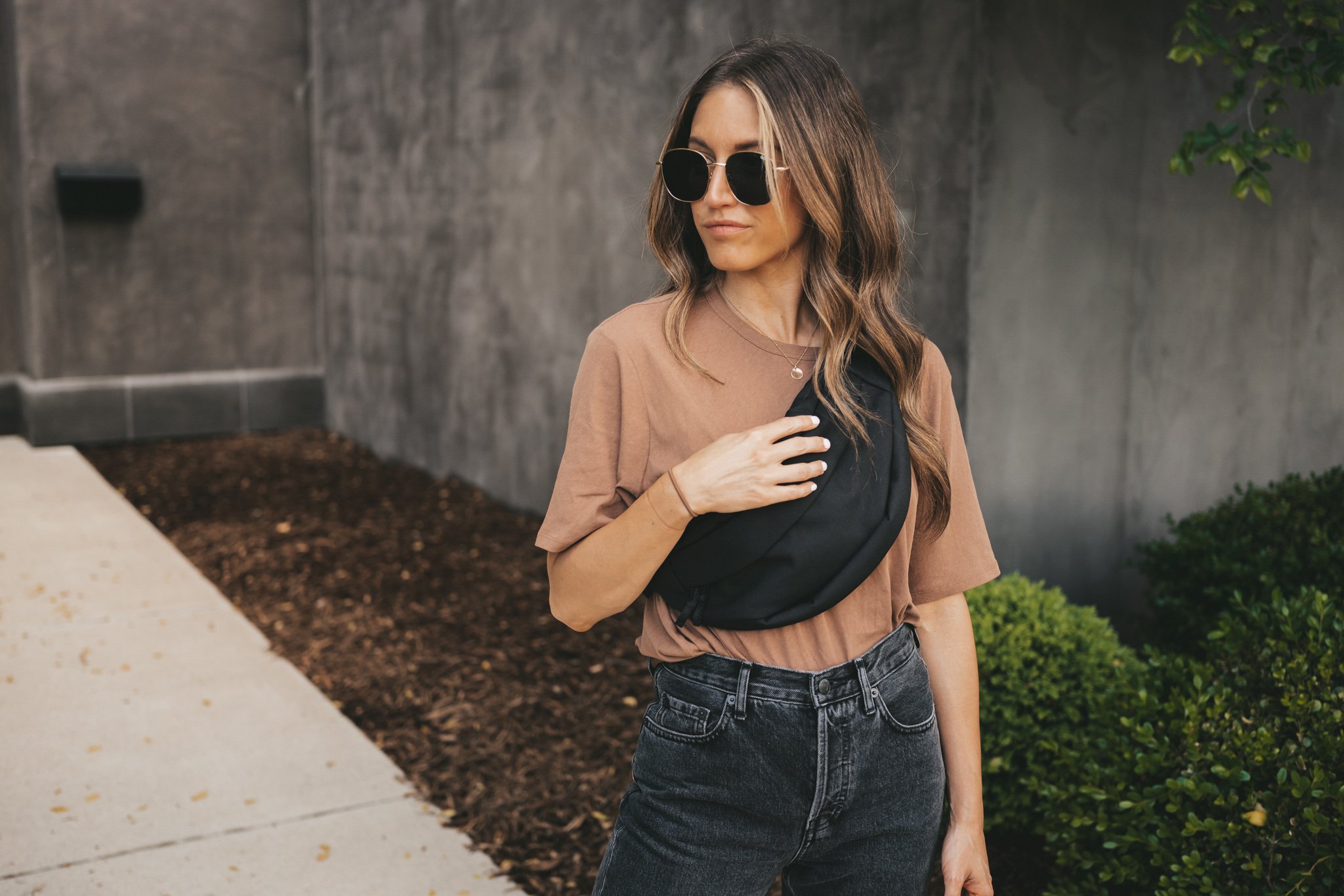 ashley wearing a basic top from Everlane, washed black straight denim, a black belt bag, and white fashion sneakers