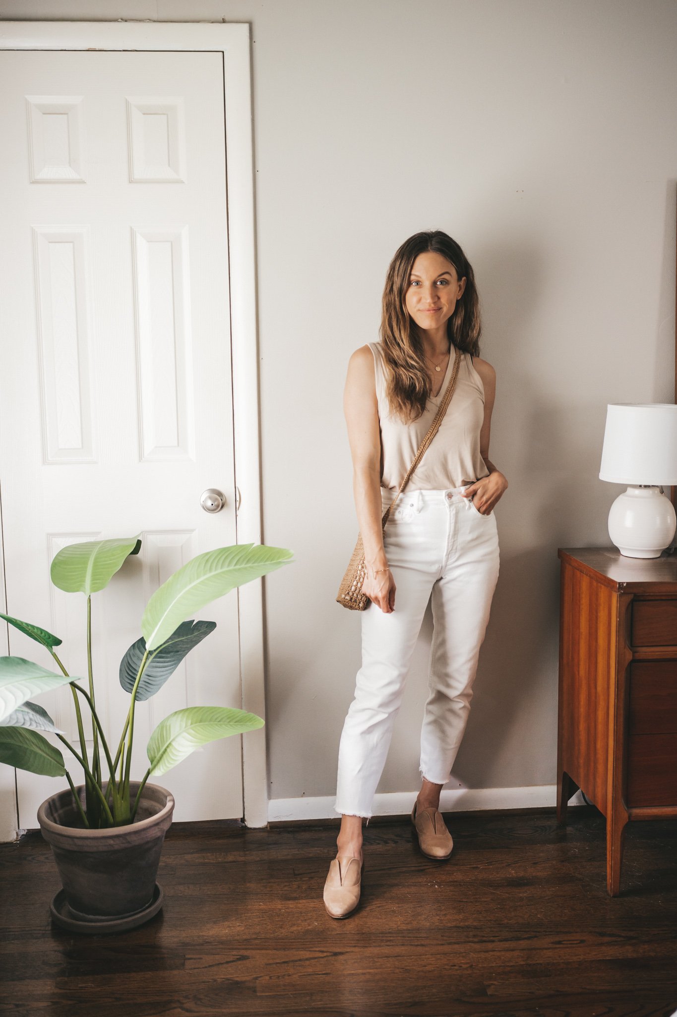ashley wearing a tan tank, white denim, and nude oxfords with a straw crossbody bag