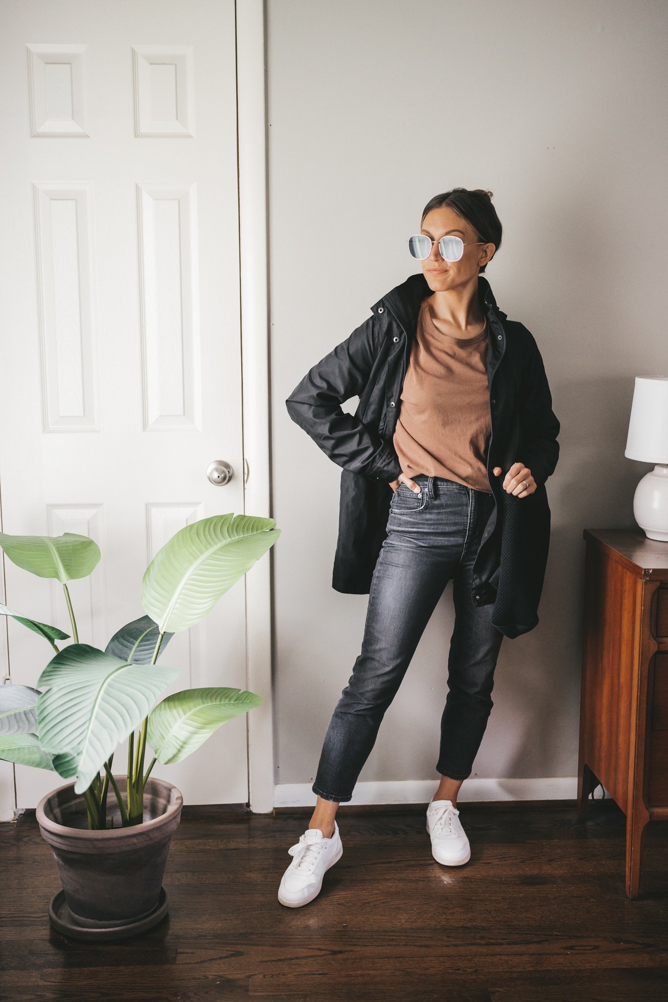 ashley wearing a brown tee, black raincoat, washed black denim, and white tennis shoes