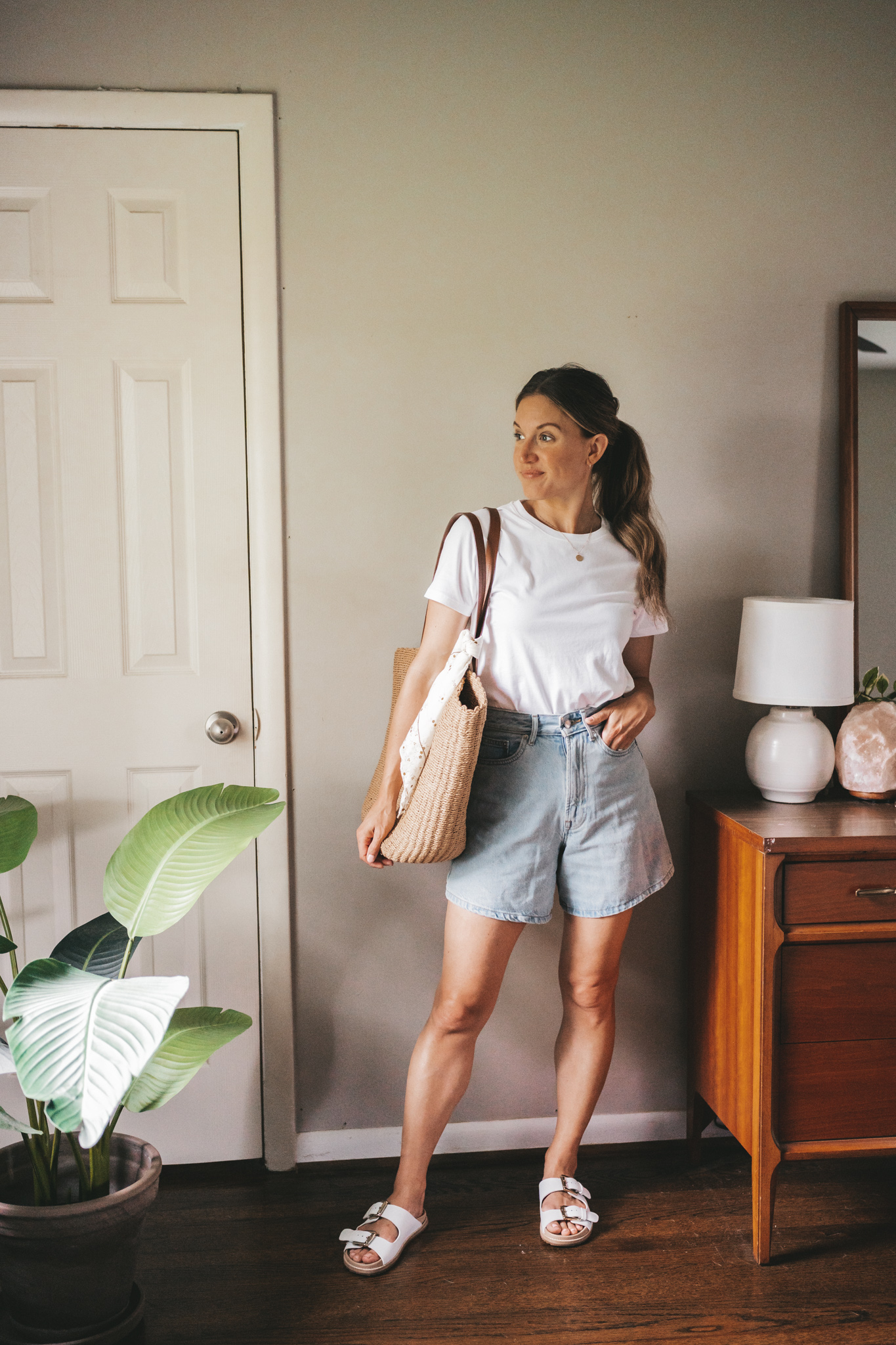 daily look with a white tee, light wash denim shorts, white sandals, and a straw tote bag