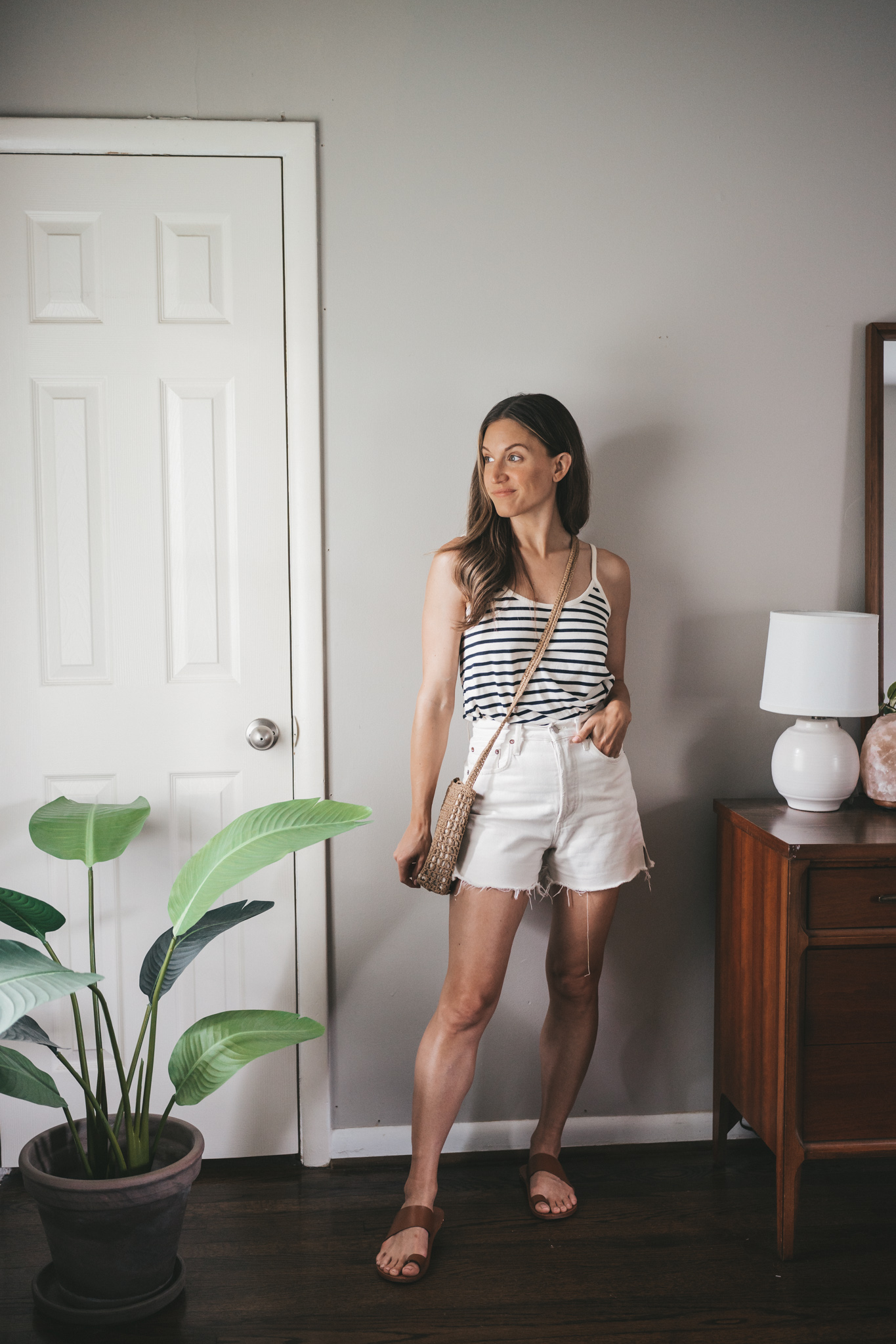 ashley wearing a striped navy and white tank, white cutoff shorts, brown leather sandals and a woven crossbody bag
