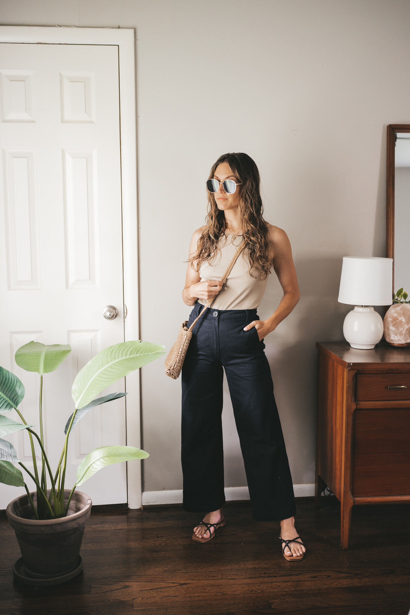 ashley wearing a taupe ribbed tank, black wide leg pants, black strappy sandals, and a straw crossbody bag