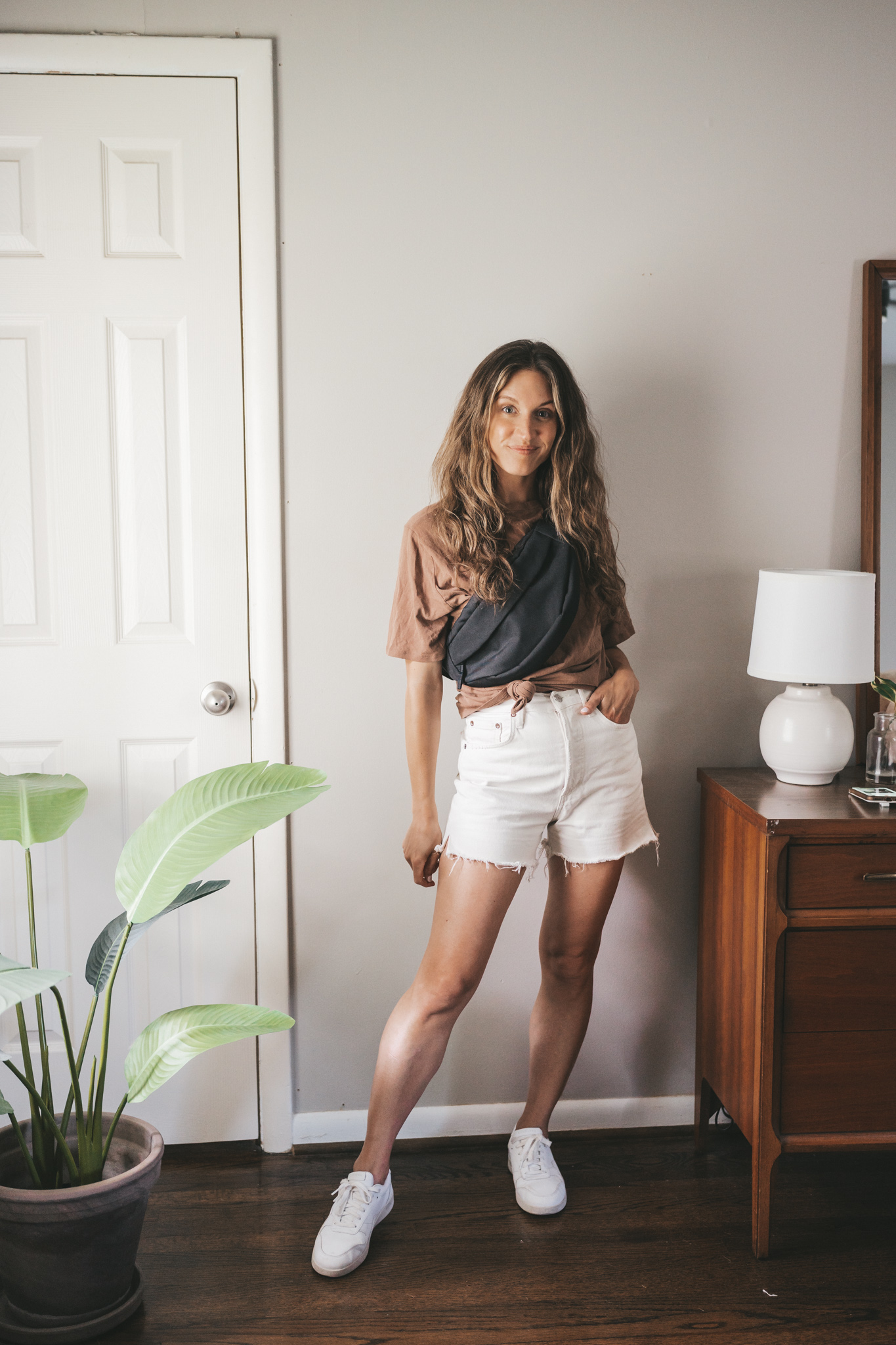ashley wearing a brown oversized tee, white denim shorts, black belt bag and white sneakers