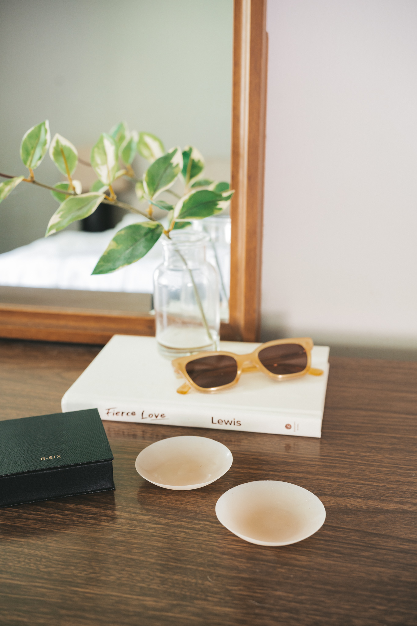 a dresser with a mirror, and a package of Nippies Nipple Covers, a white book, a pair of sunglasses, and a vase with a faux plant stem