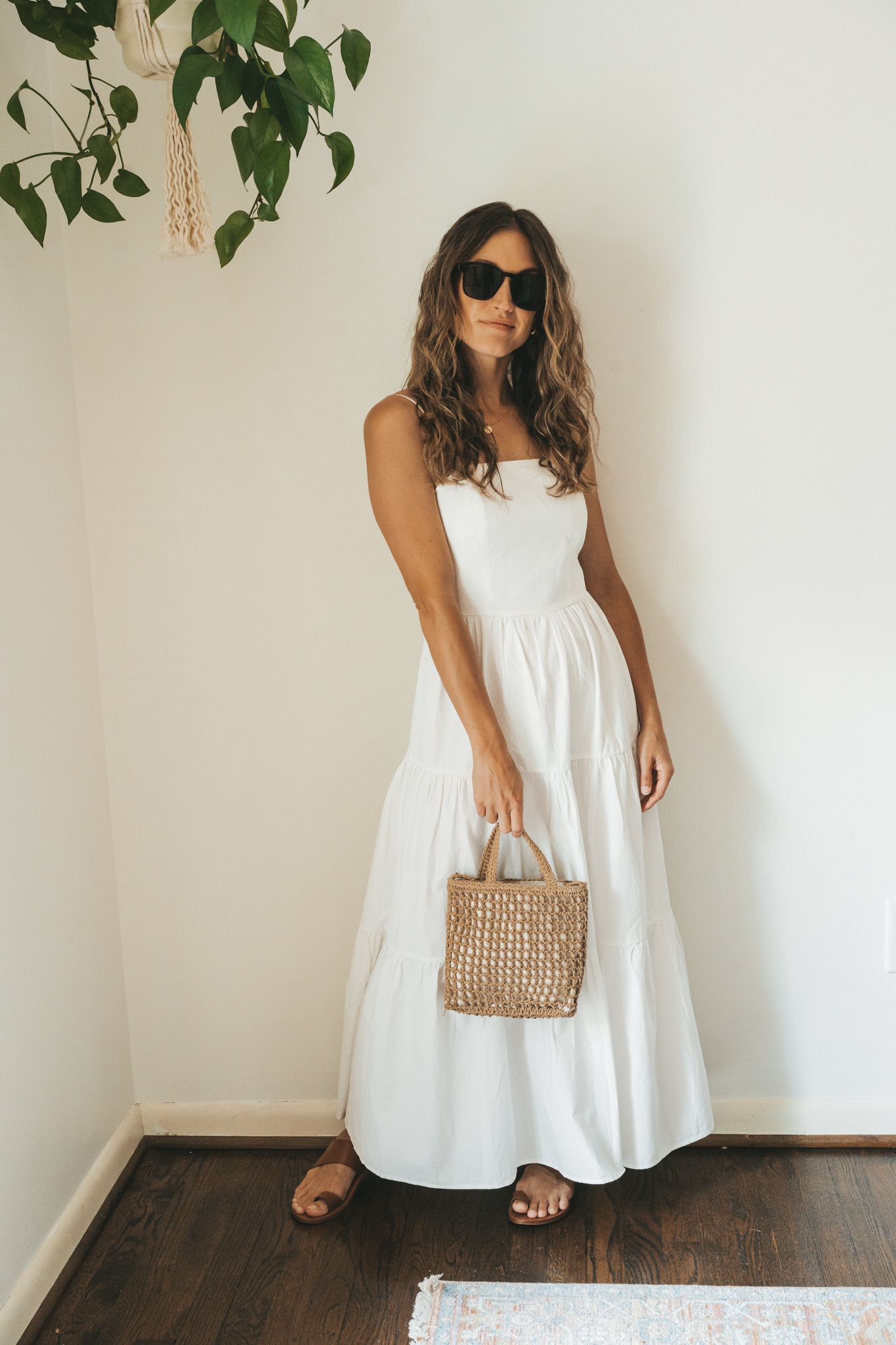ashley wearing a white tiered dress with brown leather toe ring sandals, a woven handbag, a gold pendant necklace, and tortoise shell sunglasses