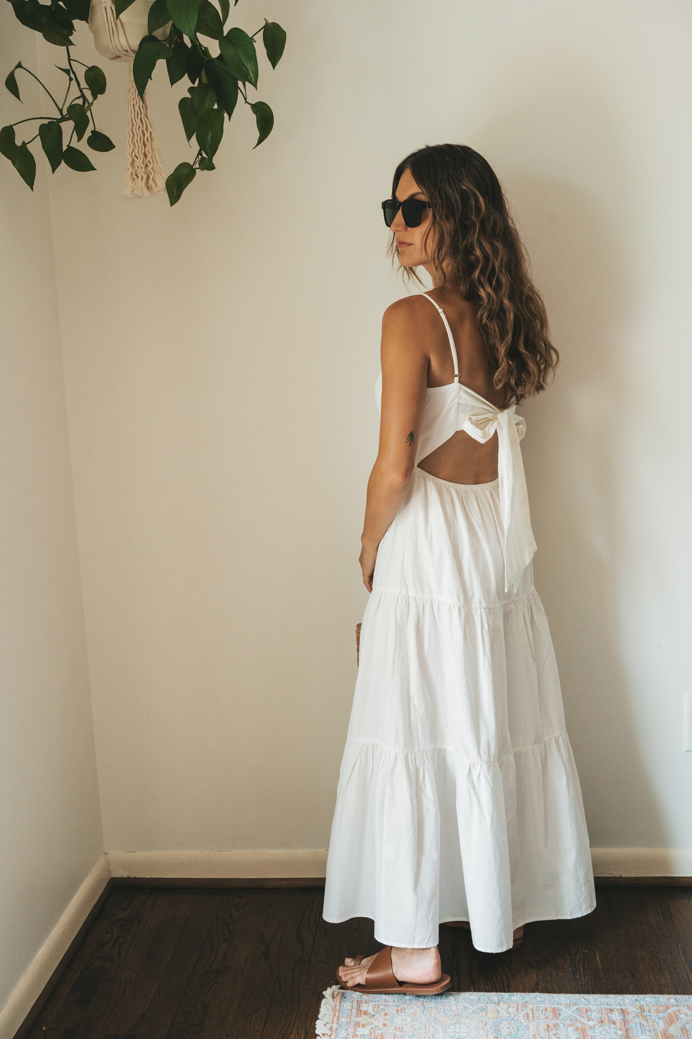 ashley wearing a white tiered dress with brown leather toe ring sandals, a woven handbag, a gold pendant necklace, and tortoise shell sunglasses