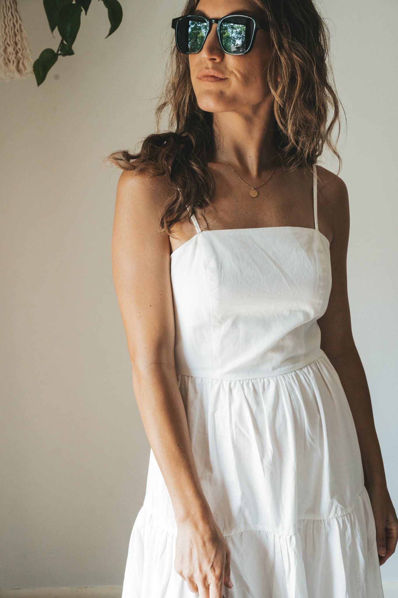ashley wearing a white tiered dress with brown leather toe ring sandals, a woven handbag, a gold pendant necklace, and tortoise shell sunglasses