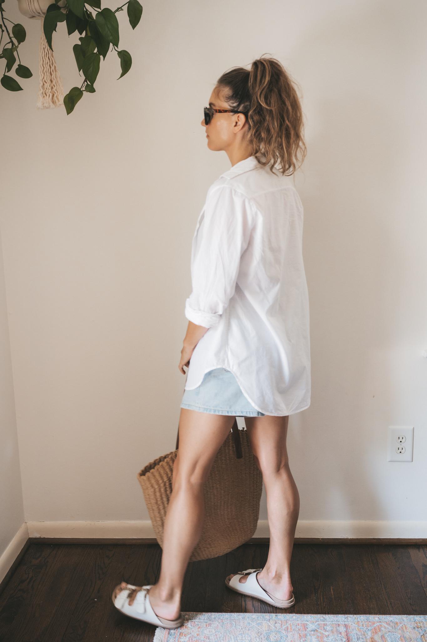 ashley wearing an olive green one piece swimsuit under a white button down, light wash denim shorts, and white sandals with tortoise shell sunglasses