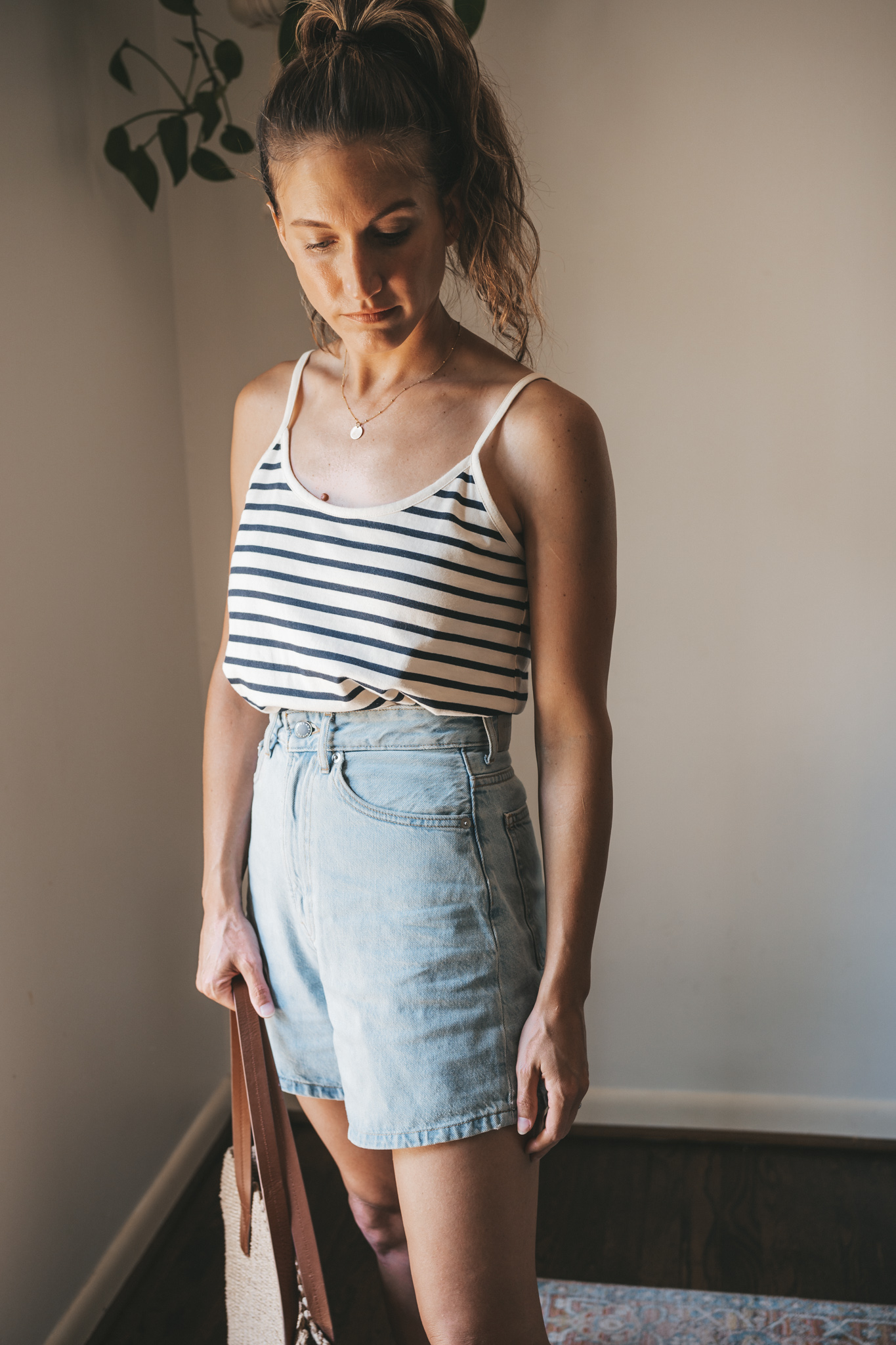 ashley wearing a striped tank, light wash denim shorts, white sandals, and a woven tote bag