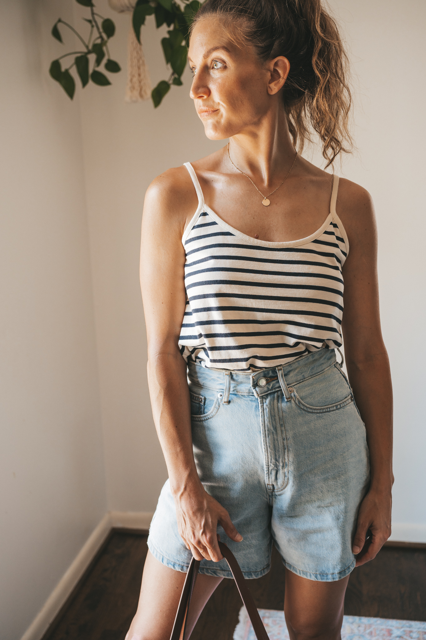 ashley wearing a striped tank, light wash denim shorts, white sandals, and a woven tote bag