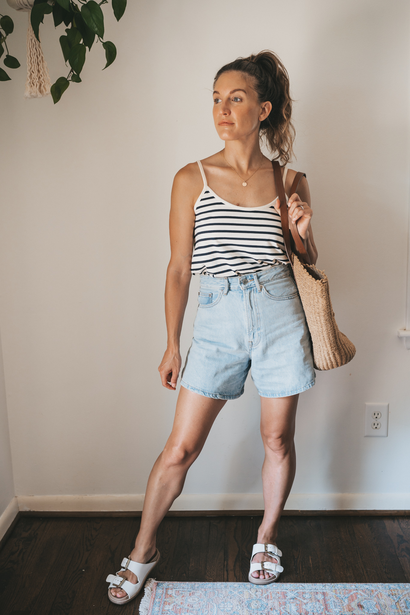 ashley wearing a striped tank, light wash denim shorts, white sandals, and a woven tote bag