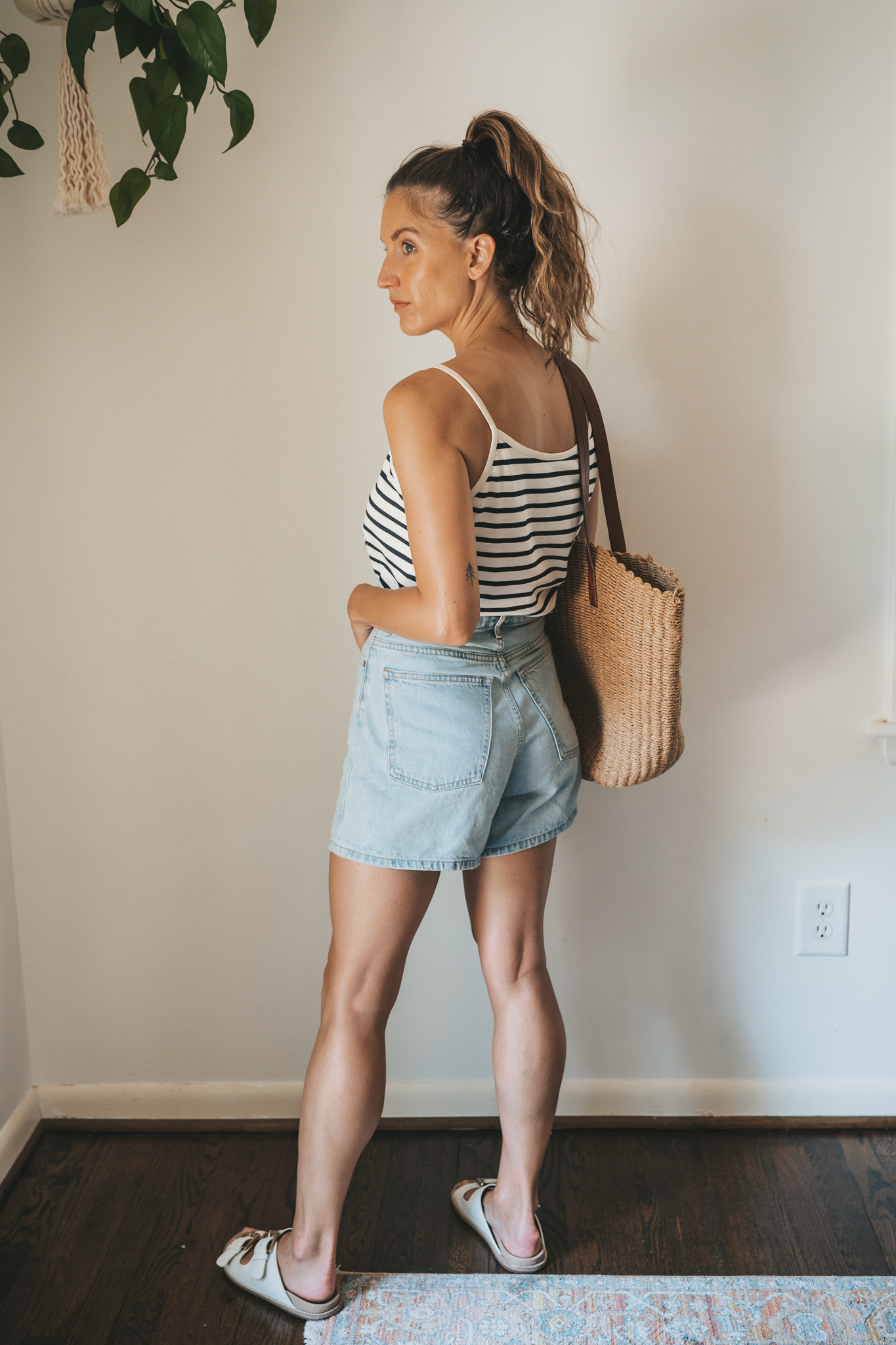 ashley wearing a striped tank, light wash denim shorts, white sandals, and a woven tote bag