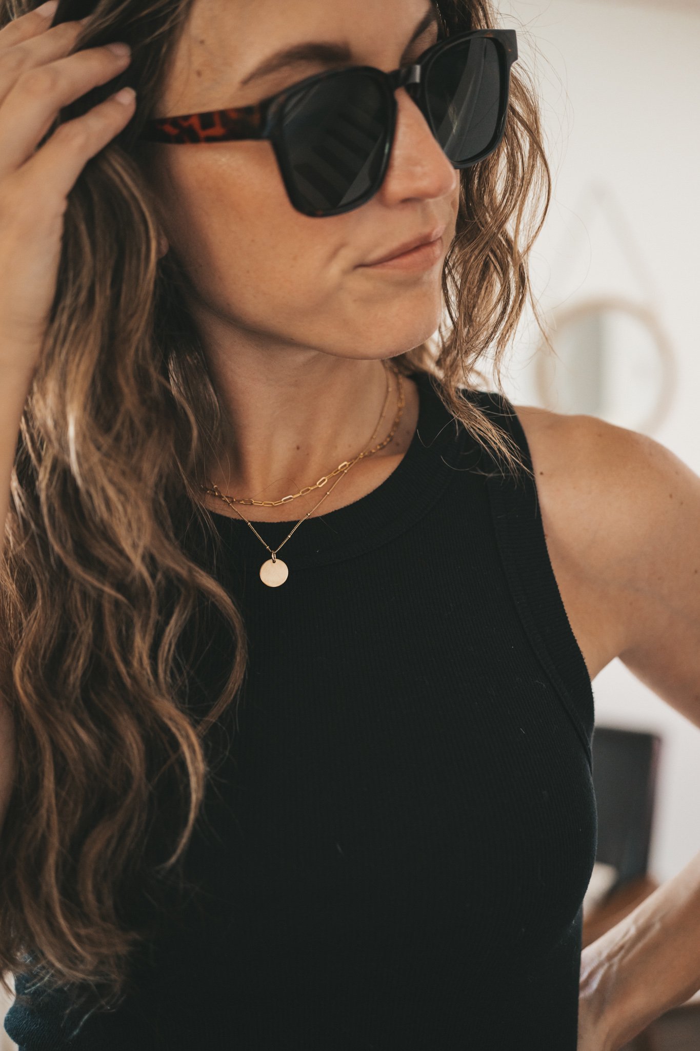 ashley wearing a black ribbed tank, black paperbag shorts, black strappy sandals, tortoise shell sunglasses, and a woven bag