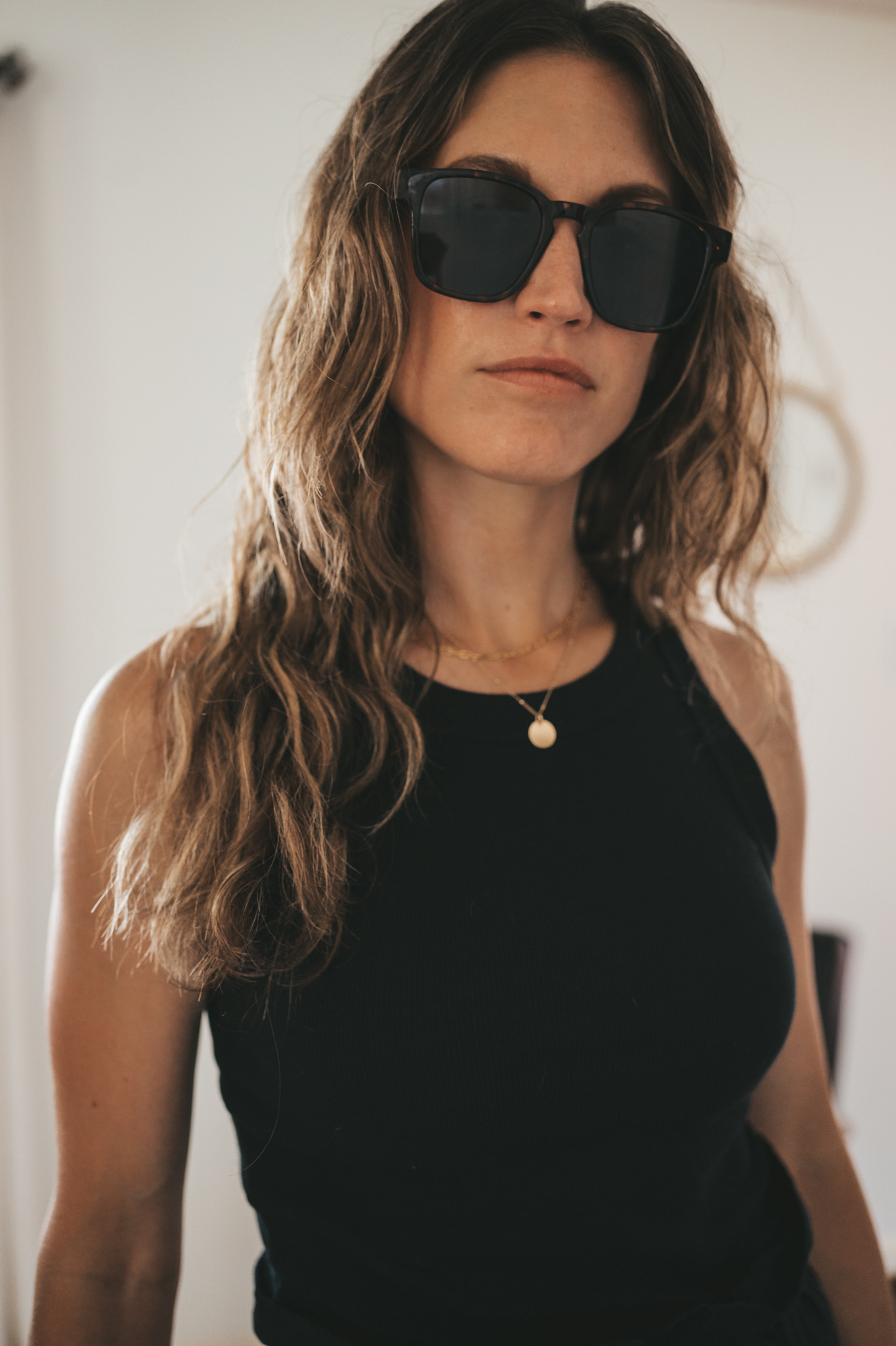 ashley wearing a black ribbed tank, black paperbag shorts, black strappy sandals, tortoise shell sunglasses, and a woven bag