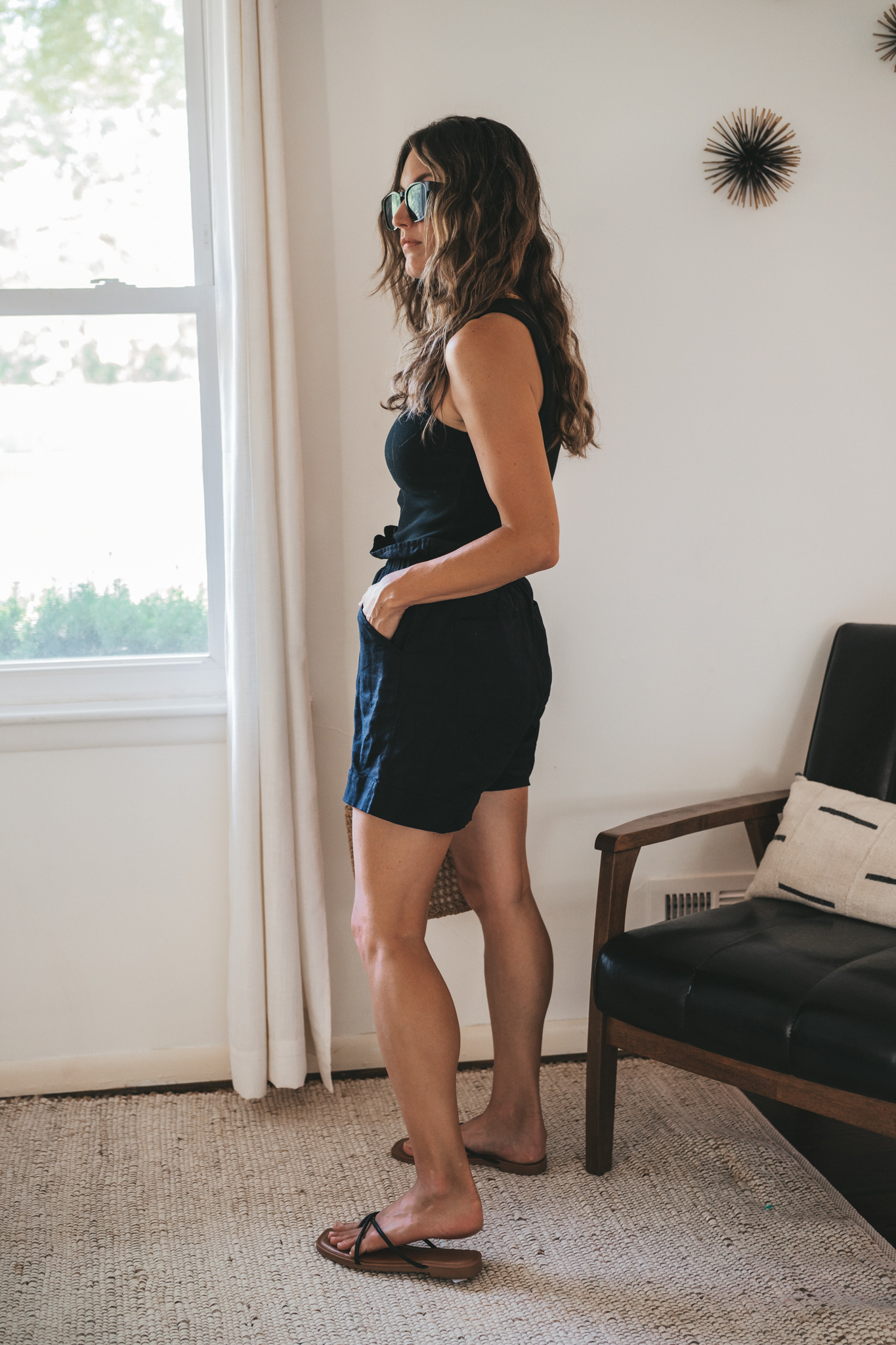 ashley wearing a black ribbed tank, black paperbag shorts, black strappy sandals, tortoise shell sunglasses, and a woven bag